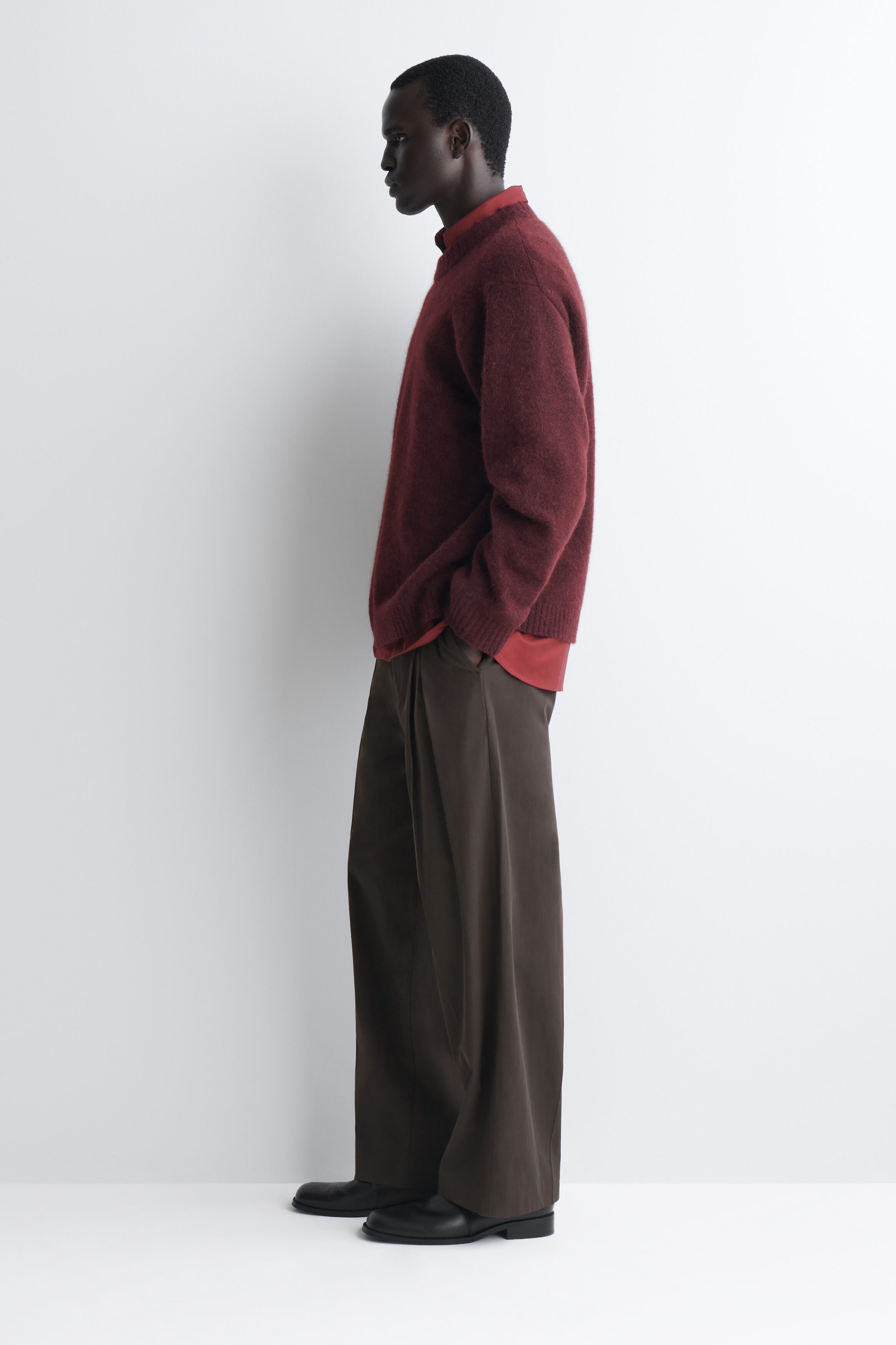 The oversized alpaca-blend crew-neck sweater in burgundy drapes loosely in a left-facing profile view, highlighting its relaxed fit and soft, brushed texture. It features ribbed cuffs and hem, and is layered over a red collared shirt visible at the neckline and hem. The oversized alpaca-blend crew-neck sweater in burgundy drapes loosely in a left-facing profile view, highlighting its relaxed fit and soft, brushed texture. It features ribbed cuffs and hem, and is layered over a red collared shirt visible at the neckline and hem.