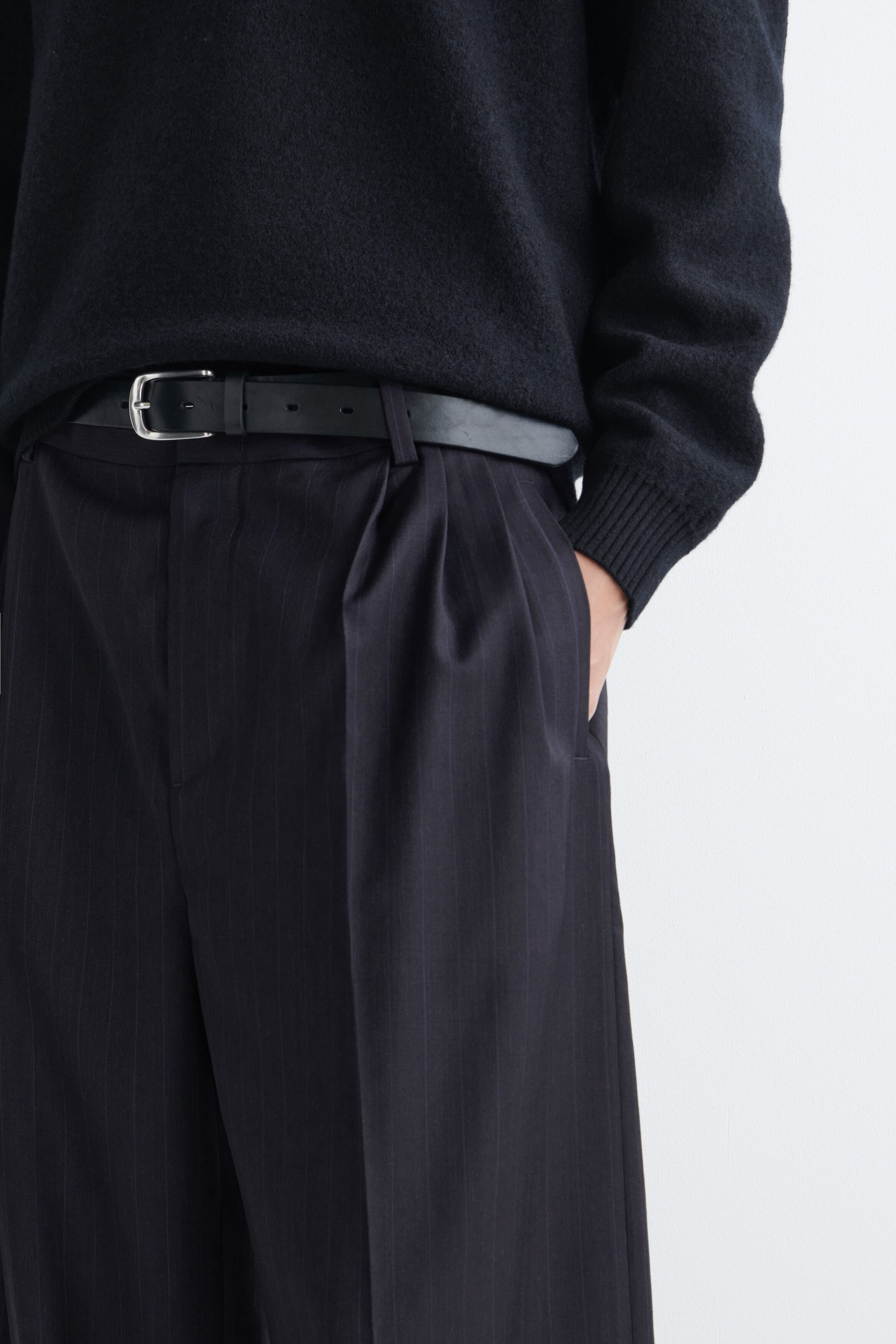 Pantalon à jambes larges à coupe décontractée avec plis, orné d’un discret motif à fines rayures et de plis sur le devant, porté par le mannequin. Le pantalon est agencé avec une ceinture en cuir noir et un chandail en tricot noir, le mannequin posant une main dans la poche latérale. Pantalon à jambes larges à coupe décontractée avec plis, orné d’un discret motif à fines rayures et de plis sur le devant, porté par le mannequin. Le pantalon est agencé avec une ceinture en cuir noir et un chandail en tricot noir, le mannequin posant une main dans la poche latérale.