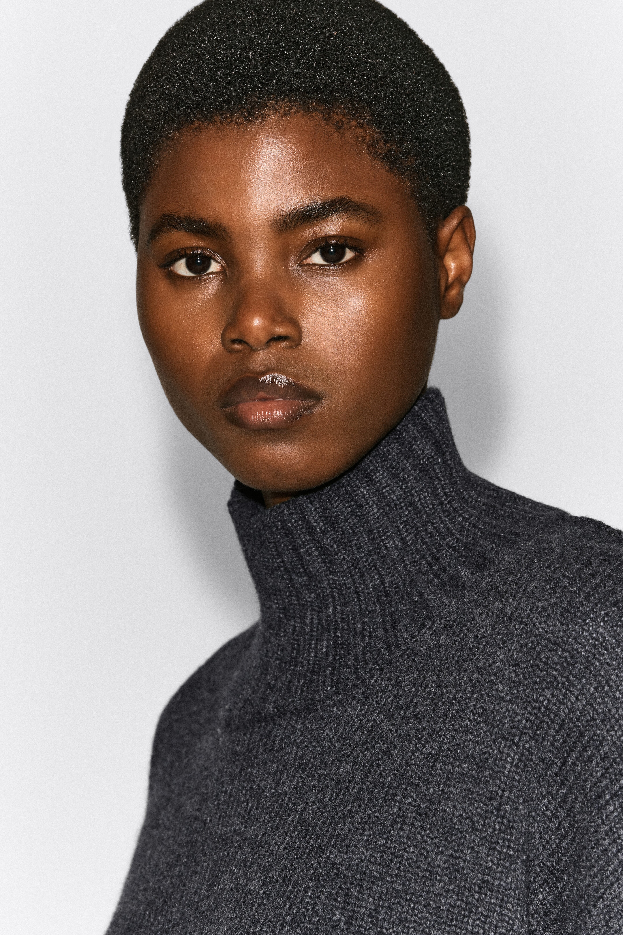 A chunky cashmere funnel-neck jumper in charcoal grey is being worn by the model in a close-up portrait. The jumper features a ribbed, high collar and a soft, textured knit structure. A chunky cashmere funnel-neck jumper in charcoal grey is being worn by the model in a close-up portrait. The jumper features a ribbed, high collar and a soft, textured knit structure.