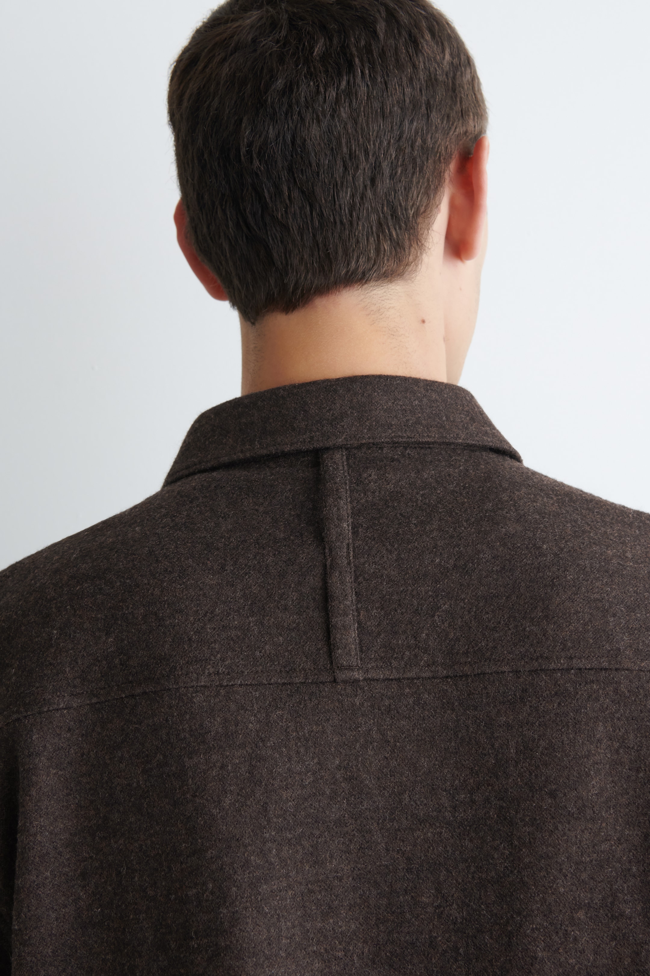 Agrandir l'image: Une surchemise texturée brun foncé est présentée de dos, avec un col classique en pointe et un empiècement arrière distinct avec un détail de couture verticale centrale.