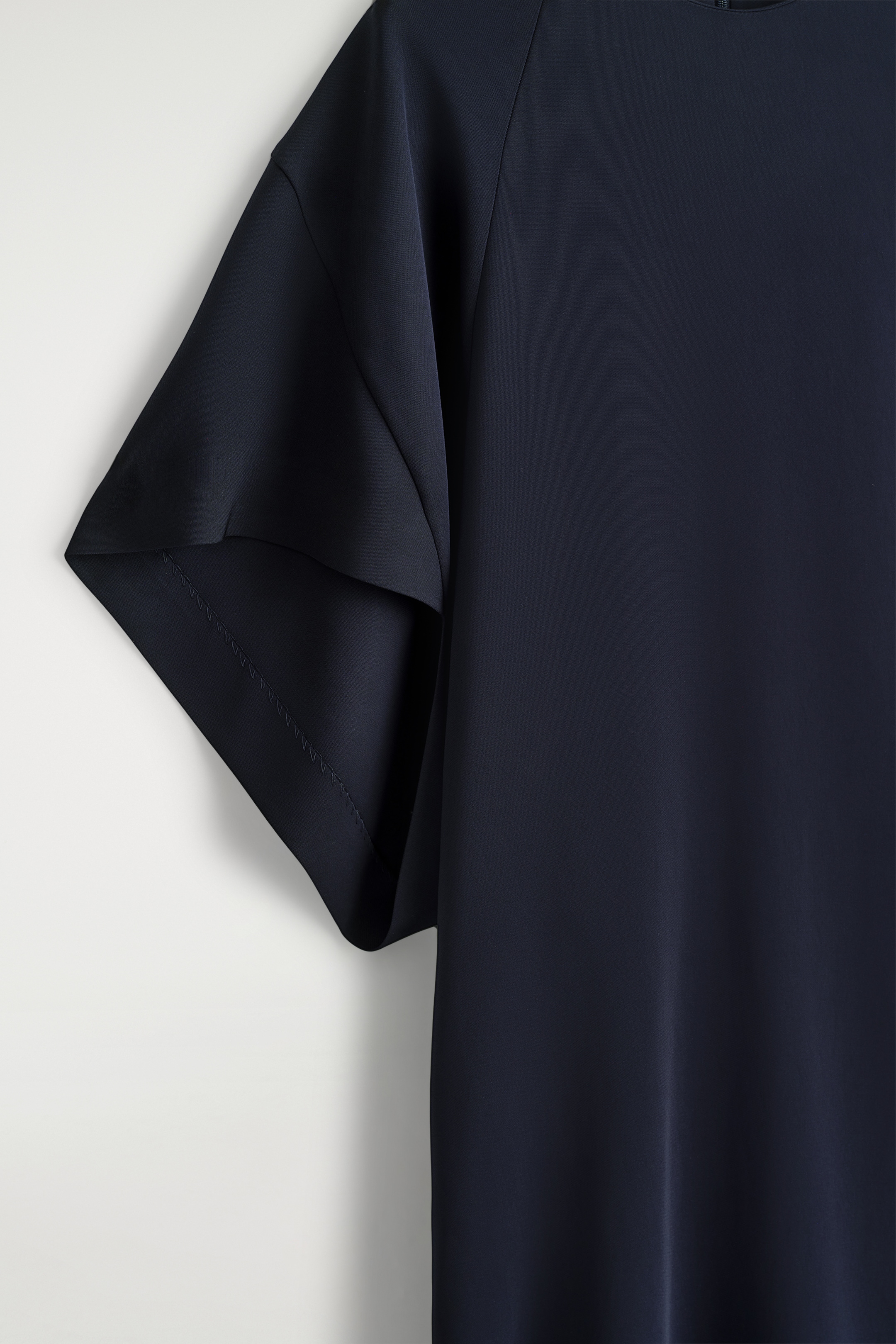 Grösseres Bild ansehen: Ein mitternachtsblaues Midikleid präsentiert seinen fließenden Viskosestoff, der sanft fällt, sowie weite, kurze Ärmel mit sichtbaren Nähten entlang des Saums.