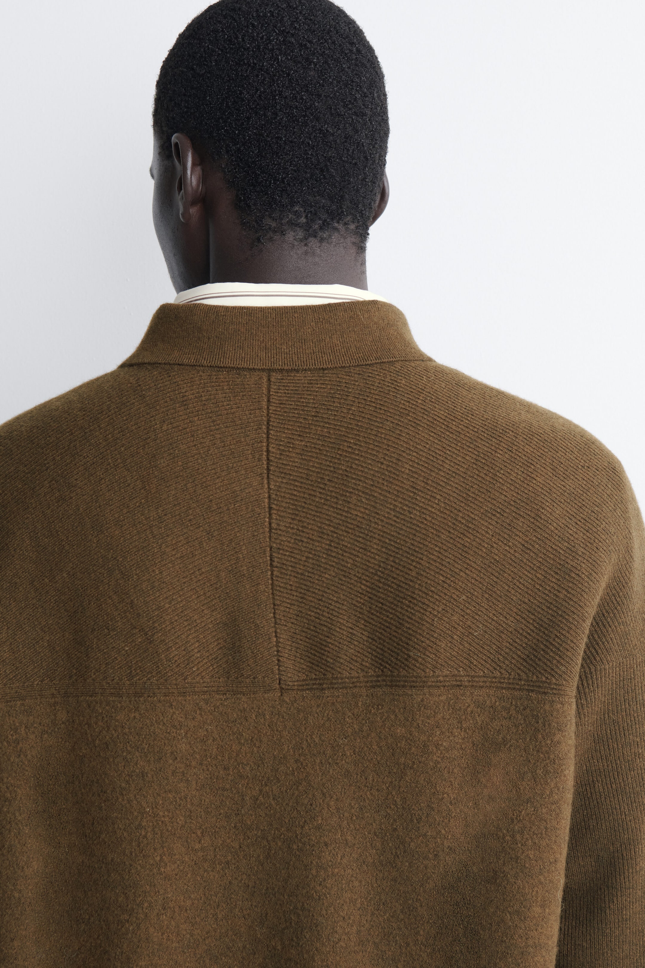 The paneled boiled-wool zip-up jumper is showing its back design, featuring a ribbed mock neck with a light-coloured shirt collar peeking out underneath. A horizontal seam divides the upper back, which showcases a diagonal-ribbed texture with a central vertical seam, from the smoother boiled-wool lower section. The paneled boiled-wool zip-up jumper is showing its back design, featuring a ribbed mock neck with a light-coloured shirt collar peeking out underneath. A horizontal seam divides the upper back, which showcases a diagonal-ribbed texture with a central vertical seam, from the smoother boiled-wool lower section.