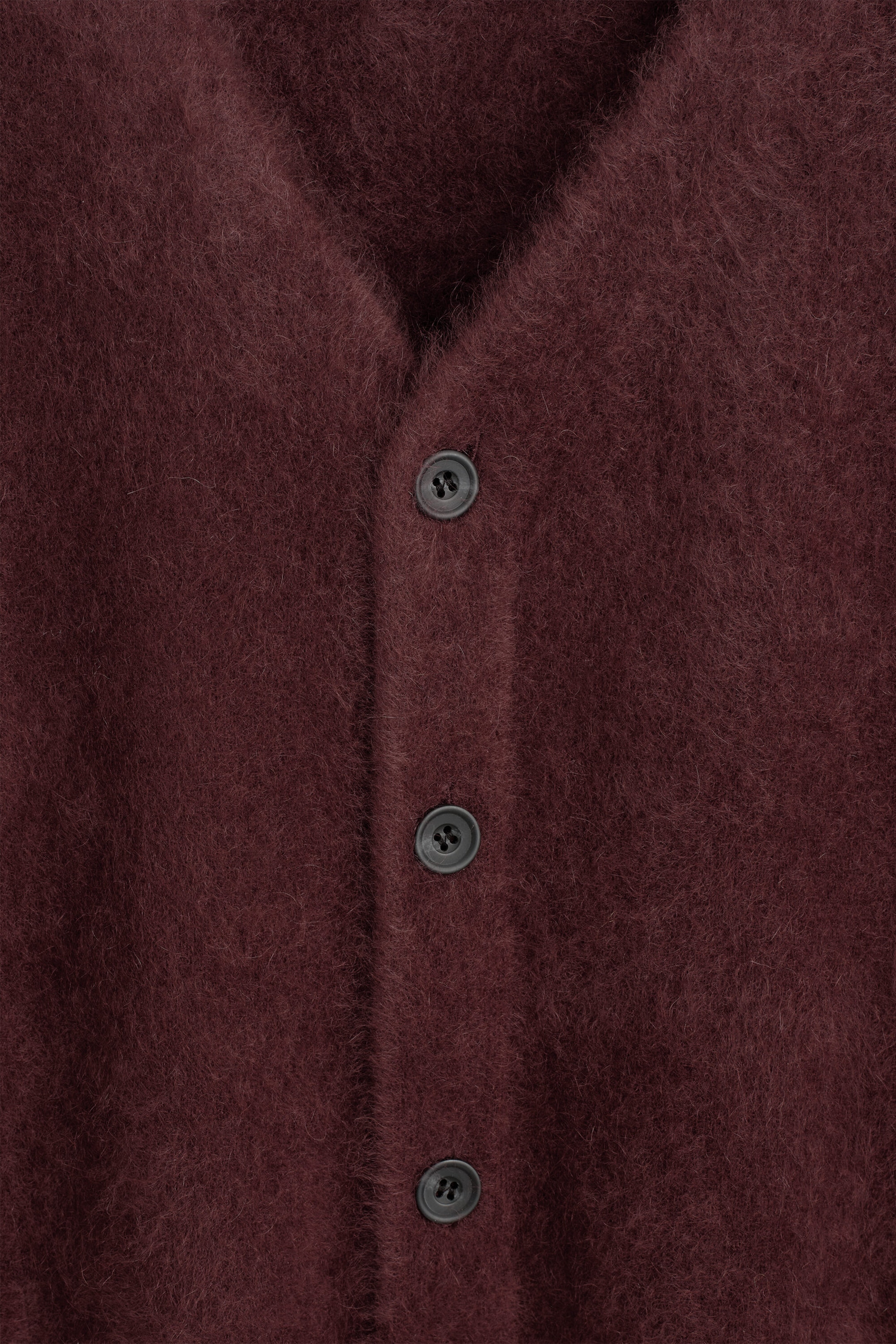 The brushed cashmere V-neck cardigan is displayed in close-up, showing its highly textured, fuzzy burgundy fabric on the front. The placket features three dark grey, four-hole buttons aligned vertically below the V-neckline. The brushed cashmere V-neck cardigan is displayed in close-up, showing its highly textured, fuzzy burgundy fabric on the front. The placket features three dark grey, four-hole buttons aligned vertically below the V-neckline.