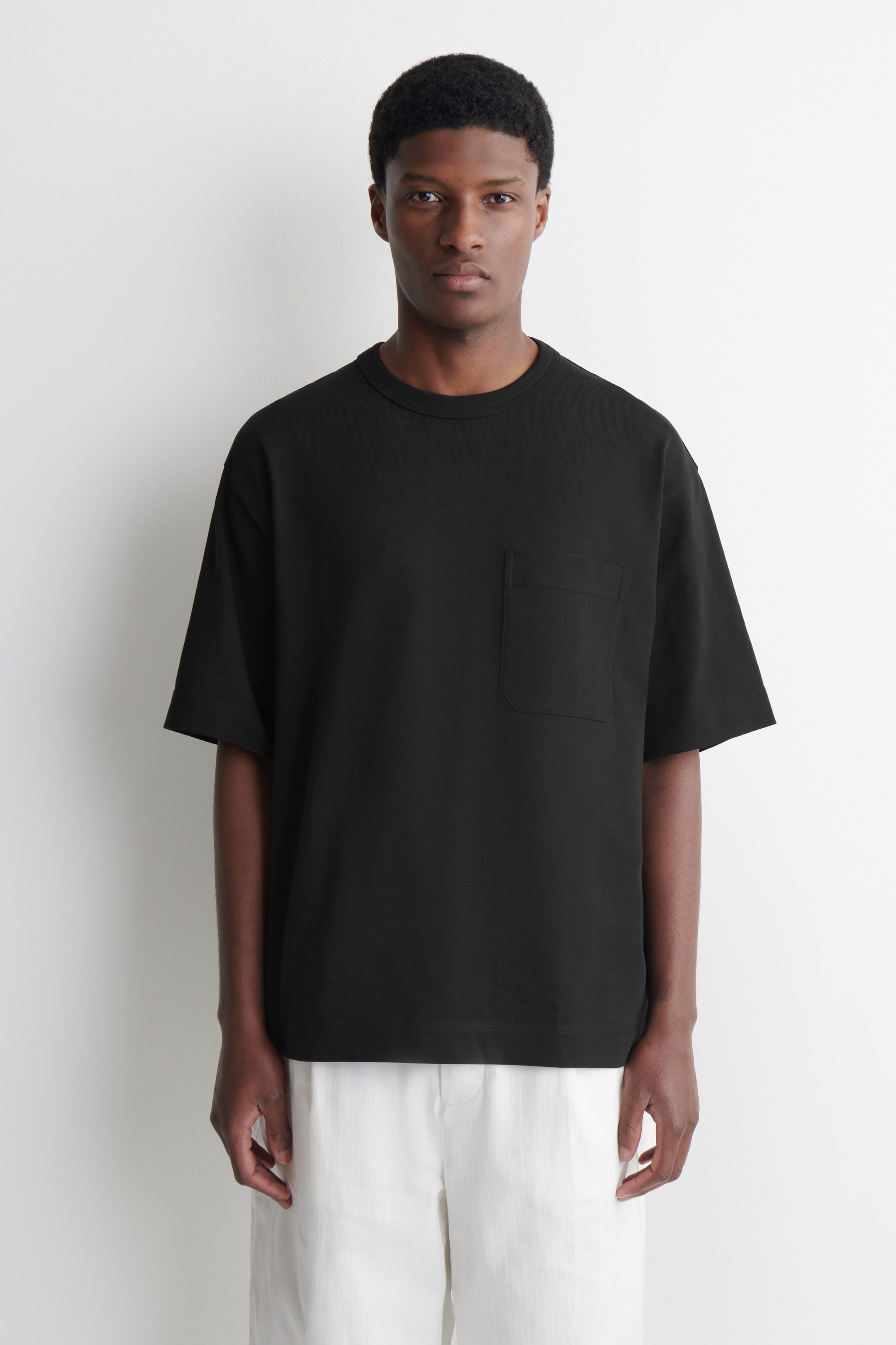 Grotere afbeelding bekijken: Een oversized zwart T-shirt wordt gedragen, naar voren gericht, met een ronde hals, korte mouwen, een borstzakje op de linkerborst en een rechte zoom, wat een ontspannen pasvorm laat zien.