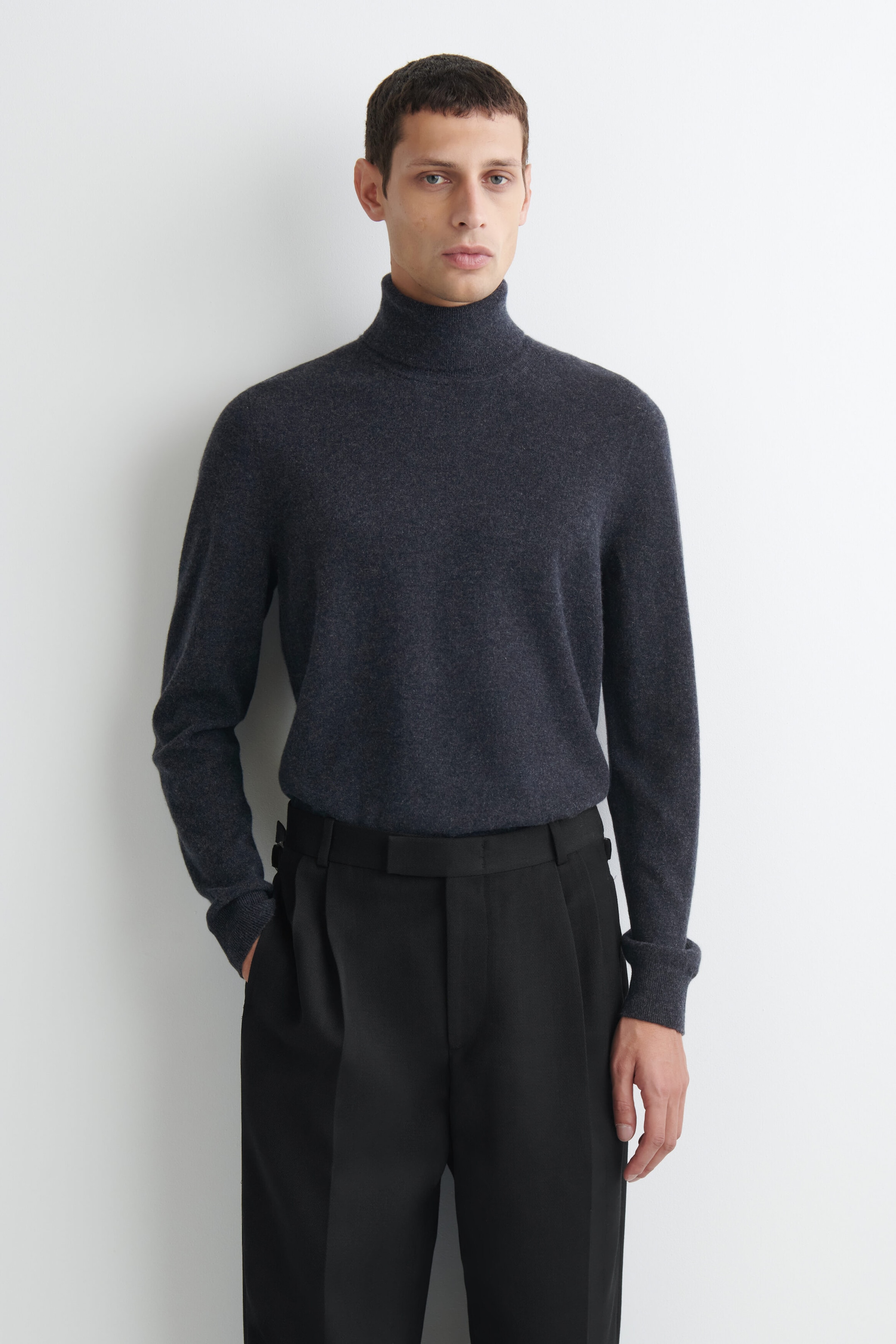 Un pull à col roulé en cachemire pur gris foncé est présenté de face, avec un col roulé montant et des manches longues à poignets côtelés. Le pull est porté rentré dans un pantalon noir structuré, mettant en valeur sa texture en maille douce et sa coupe régulière. Un pull à col roulé en cachemire pur gris foncé est présenté de face, avec un col roulé montant et des manches longues à poignets côtelés. Le pull est porté rentré dans un pantalon noir structuré, mettant en valeur sa texture en maille douce et sa coupe régulière.