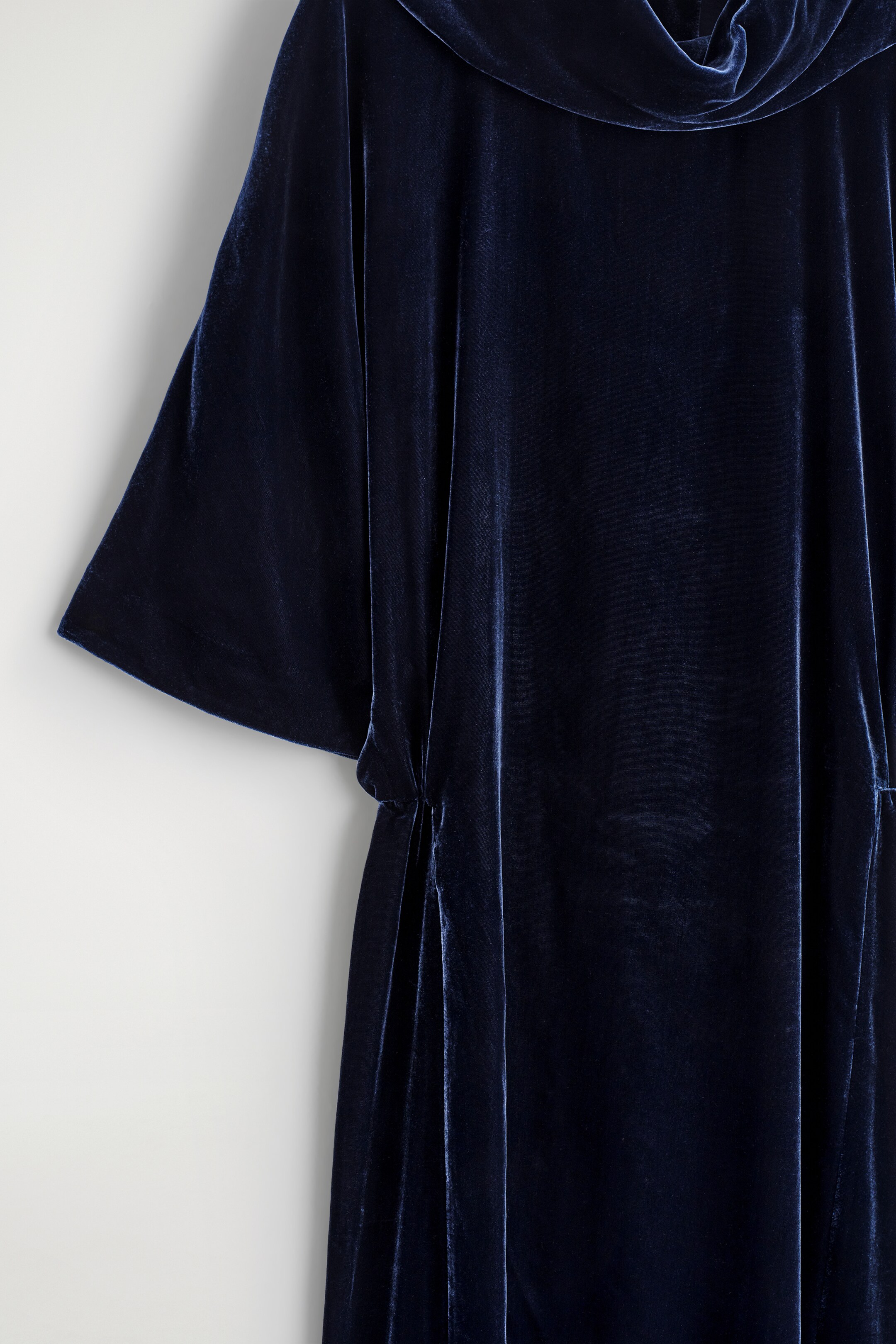 Ver imagem maior: O vestido de veludo azul-marinho apresenta um colarinho alto drapeado, uma manga larga estilo morcego e um detalhe franzido na lateral que confere uma cintura blouson.
