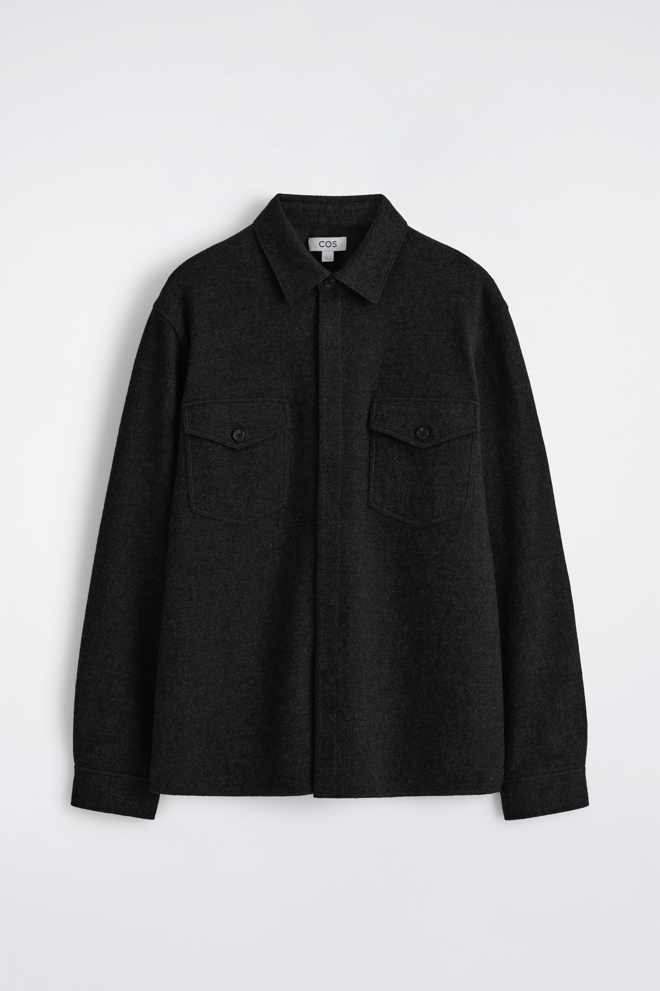 Visualizza immagine più grande: Un'overshirt grigio scuro è presentata frontalmente, caratterizzata da un colletto a punta e una paramontura coperta. Presenta due tasche con patta sul petto con chiusure a bottone e una vestibilità comoda, con il tessuto che esibisce una consistenza tattile, bollita.