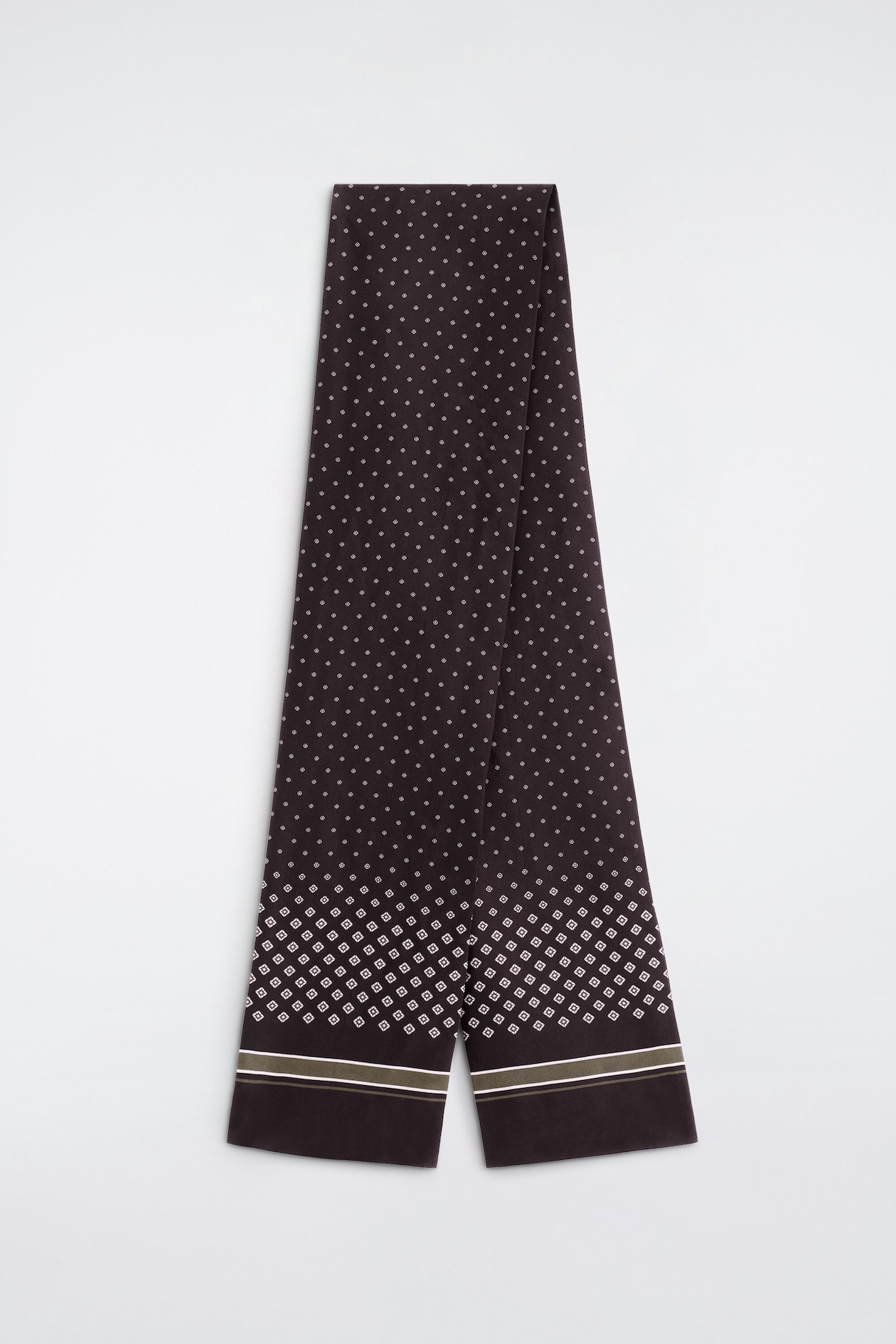 A slim, elongated dark brown silk scarf is hanging folded in half, displaying a repeating white micro-diamond motif across its body. The bottom sections feature a denser geometric diamond pattern above horizontal olive-green and white stripes, with solid dark brown ends.