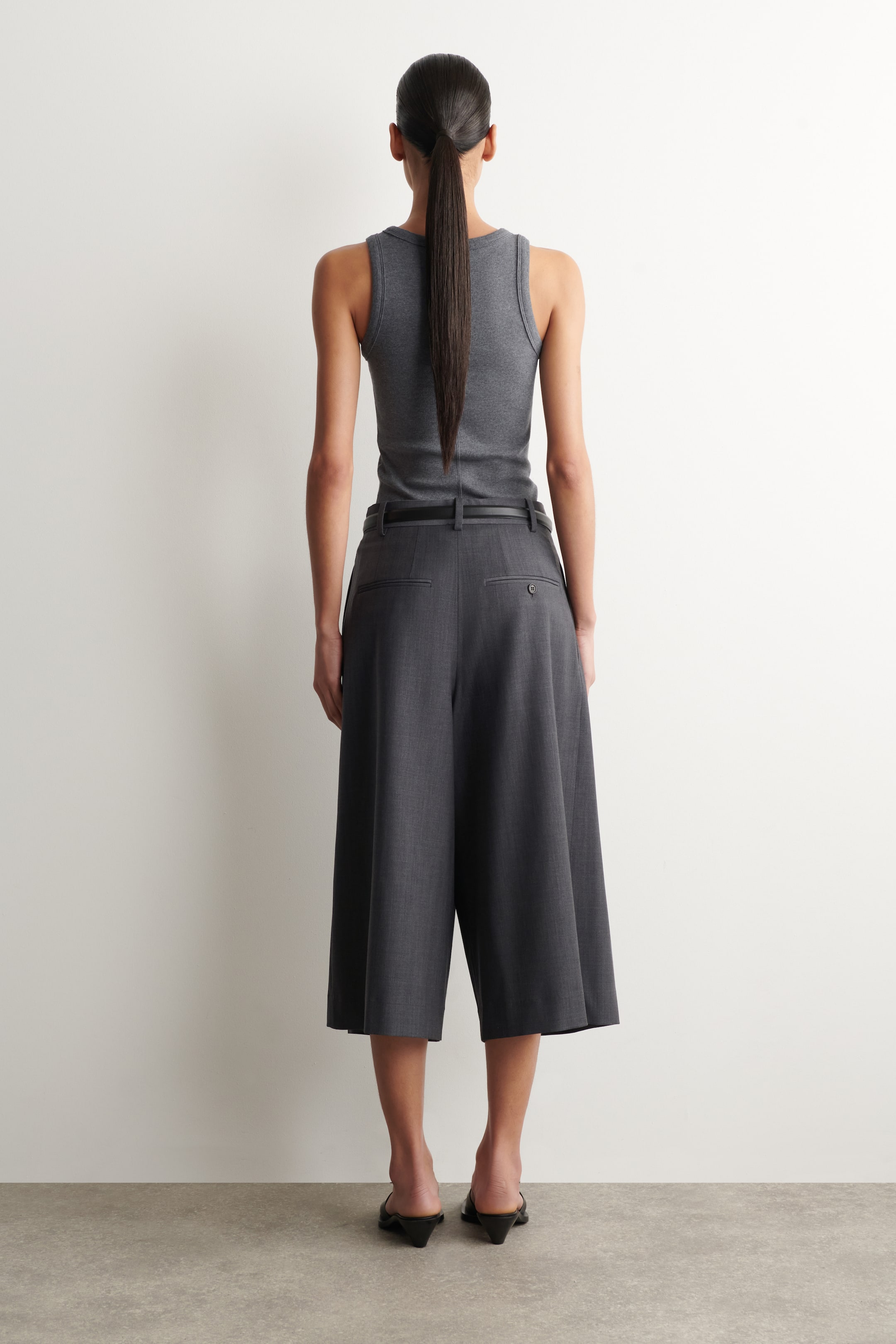 Visualizza l'immagine ingrandita: Un top grigio a costine e pantaloni cropped a gamba larga in grigio scuro sono presentati dal retro. I pantaloni presentano passanti per cintura e due tasche posteriori, e una sottile cintura nera è infilata attraverso di essi.