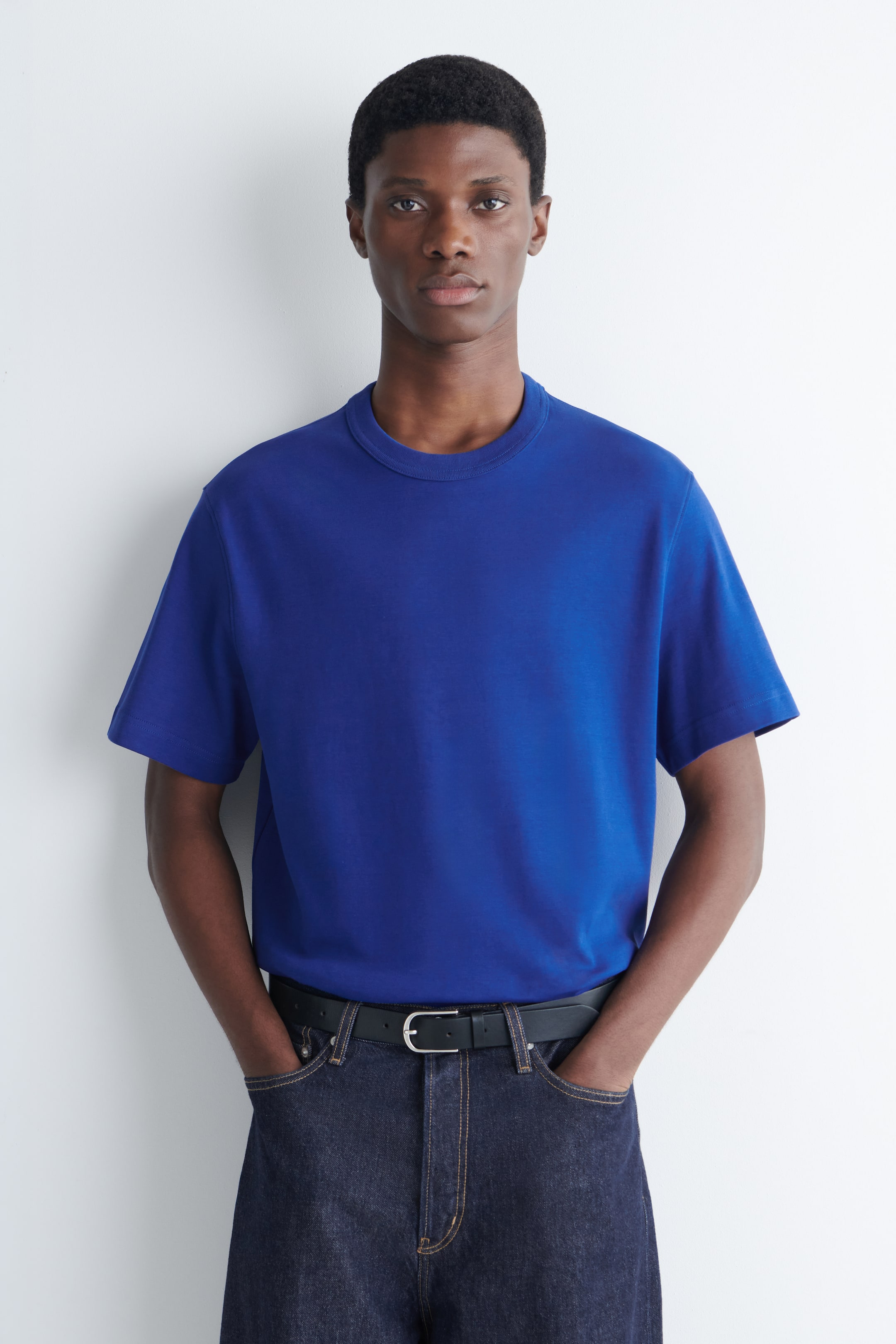 Größeres Bild ansehen: Ein blaues T-Shirt mit Rundhalsausschnitt, kurzen Ärmeln und einer lockeren Passform wird von dem Model getragen.