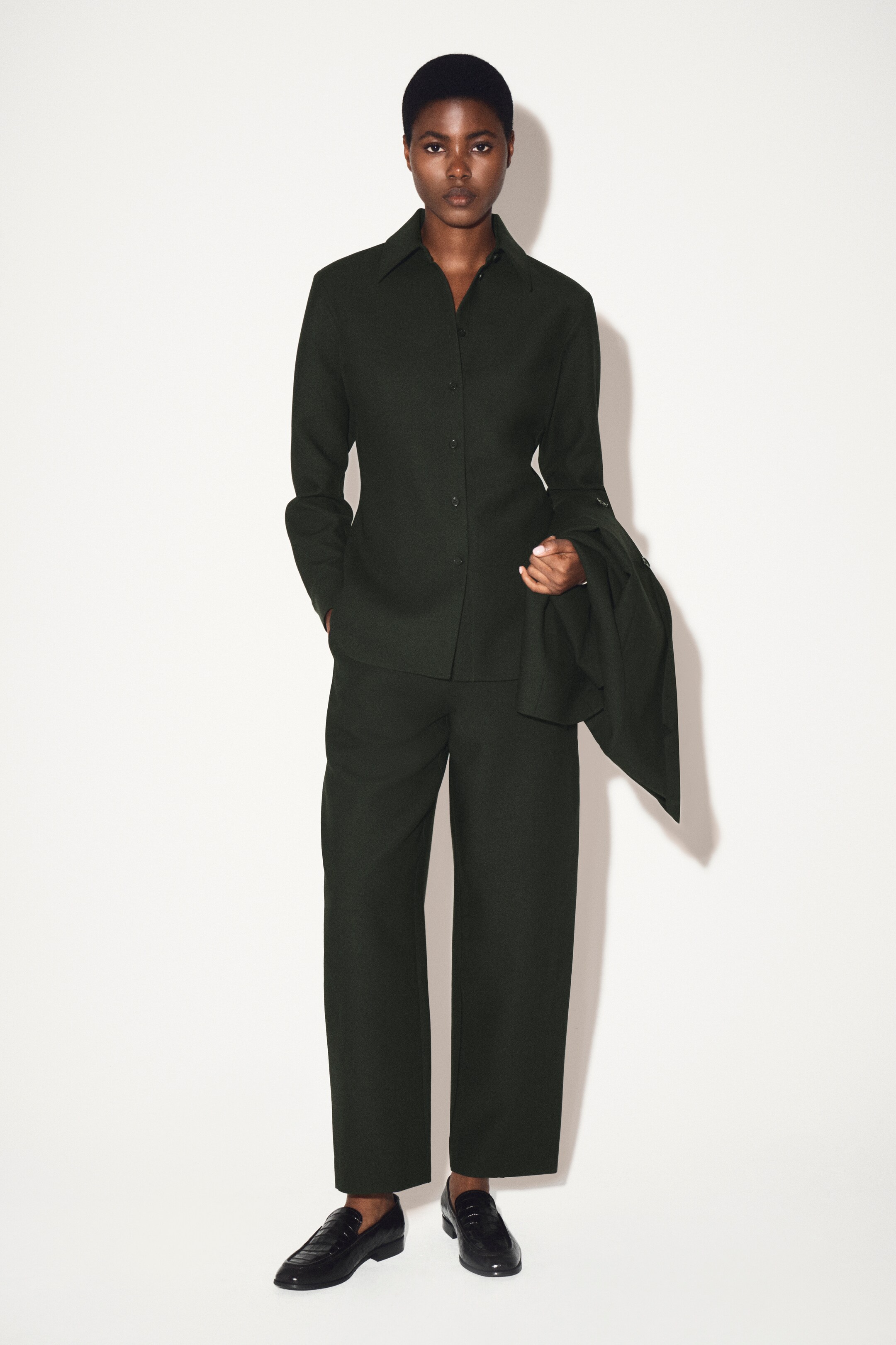 Größeres Bild anzeigen: RELAXIERTES WOLLSHIRT. Dieses dunkelgrüne Wollhemd wird von vorne präsentiert und zeigt einen spitzen Kragen sowie eine durchgehende Knopfleiste mit dunklen Knöpfen. Es zeigt auch lange Ärmel, die in Knopfmanschetten enden.