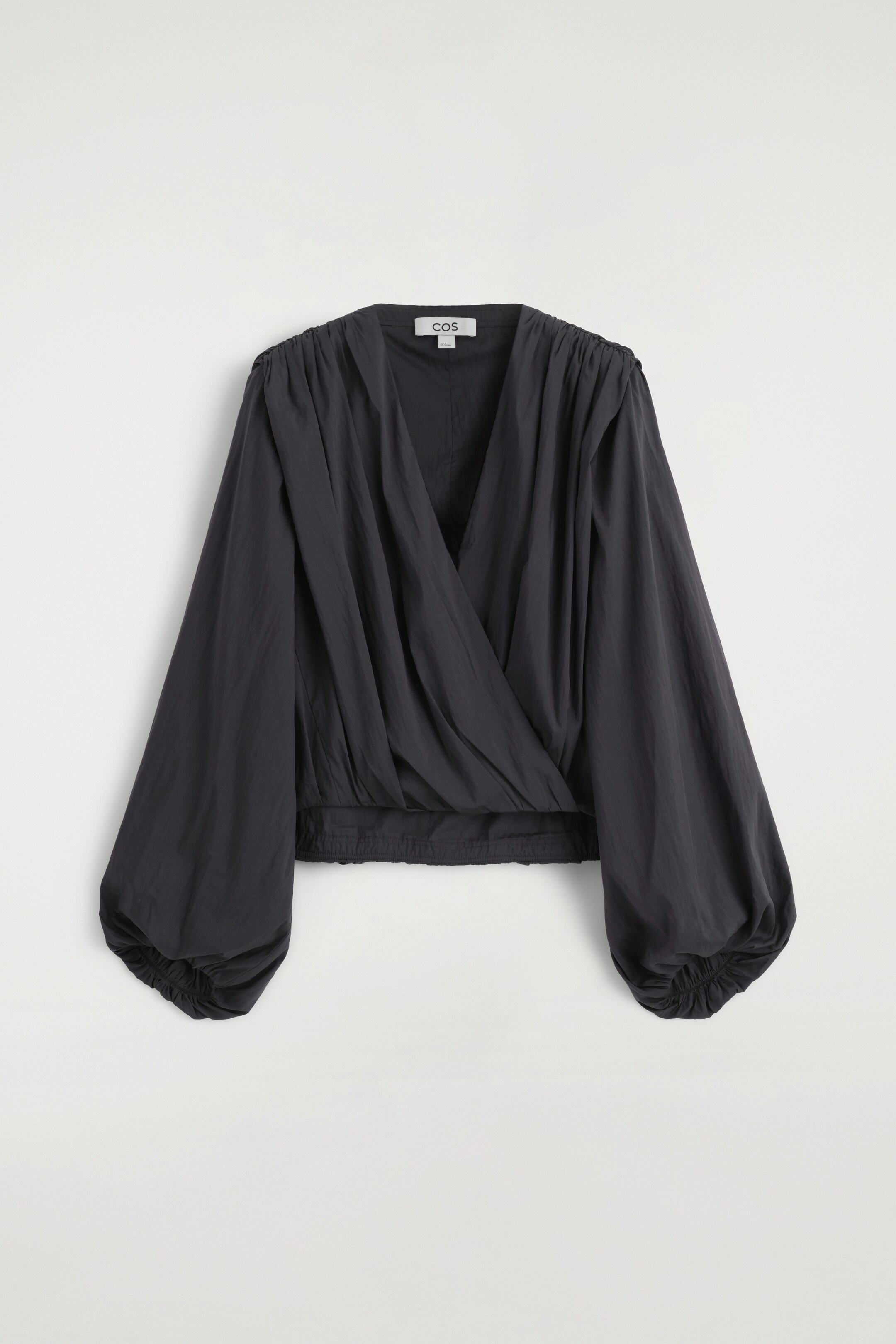 Agrandir l'image: Une blouse cache-coeur gris foncé présente son devant, avec un décolleté en V profond et des épaules froncées. Ses longues manches bouffantes se resserrent avec des poignets élastiqués, et la blouse se termine par un ourlet froncé et élastiqué.