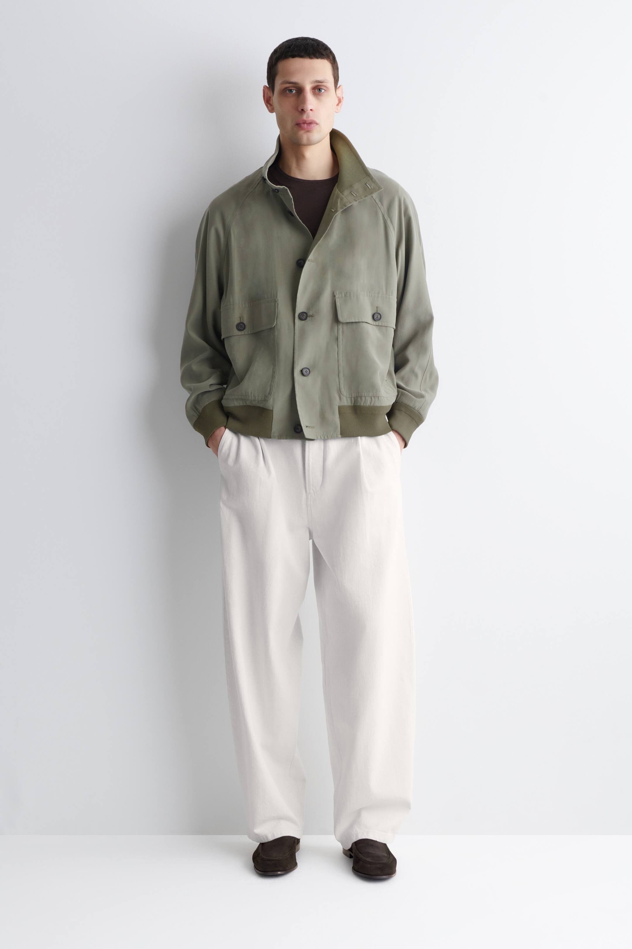 View larger image: The item is an olive green bomber jacket, off-white wide-leg trousers, and dark brown loafers, all showcased from the front. The jacket features a button-down front with two flap chest pockets, a standing collar, and contrasting ribbed cuffs and hem, worn over a dark brown t-shirt.