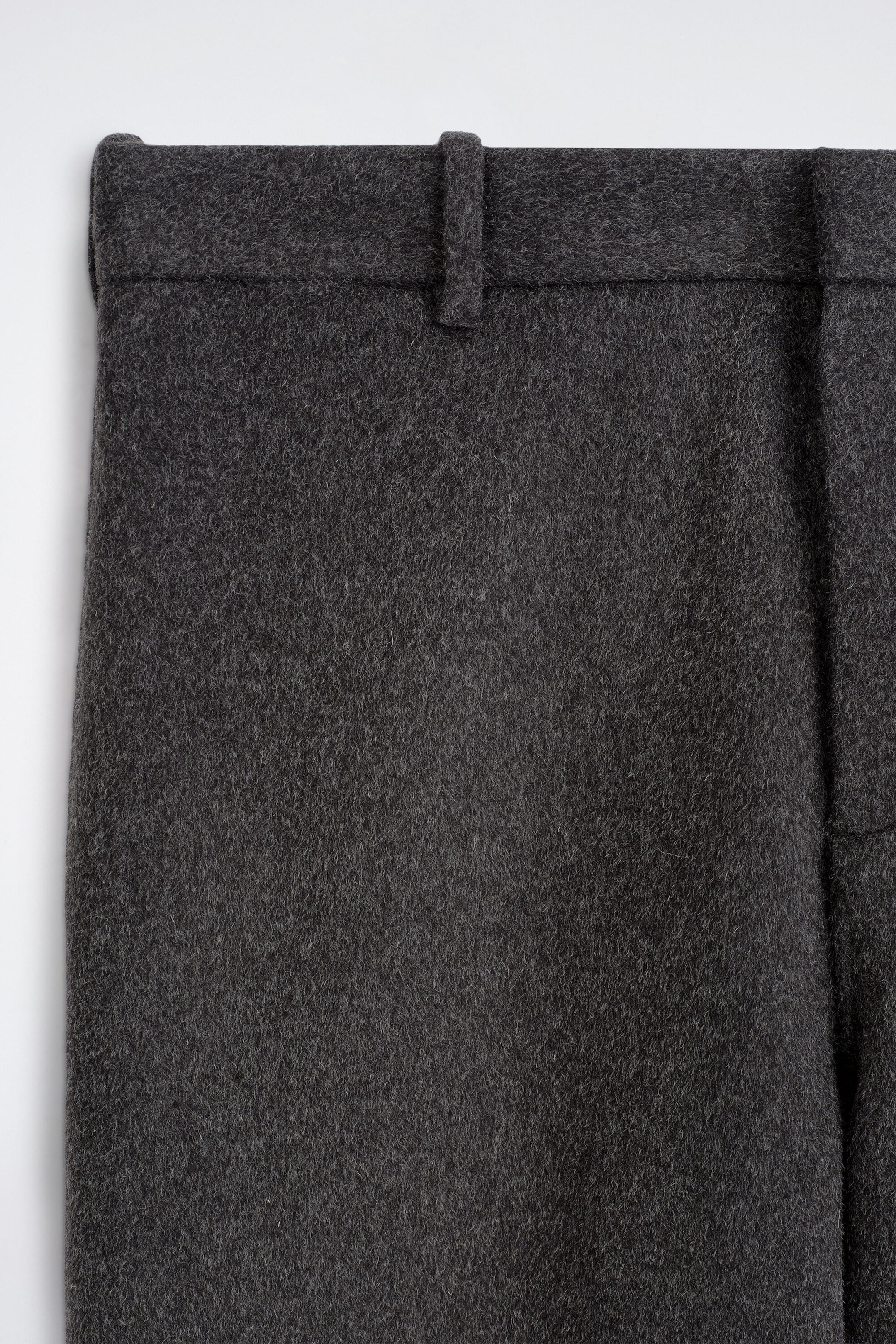Die doppelseitige Wollhose mit lockerer Passform und weitem Bein wird in einer nahen Frontalansicht gezeigt und hebt das dunkelgraue, strukturierte Wollmaterial, den formstabilen Bund und eine einzelne Gürtelschlaufe hervor. Die doppelseitige Wollhose mit lockerer Passform und weitem Bein wird in einer nahen Frontalansicht gezeigt und hebt das dunkelgraue, strukturierte Wollmaterial, den formstabilen Bund und eine einzelne Gürtelschlaufe hervor.