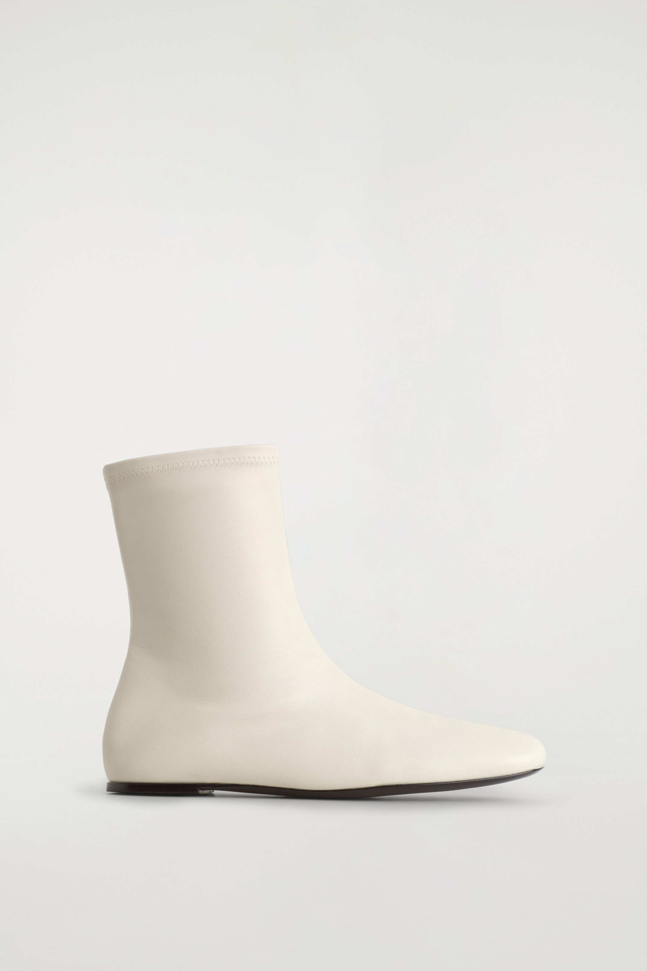 View larger image: A single cream leather sock boot is facing right, presenting a slim shape with a rounded square toe. It is featuring a smooth, chalk-toned upper and a low, flat dark sole.