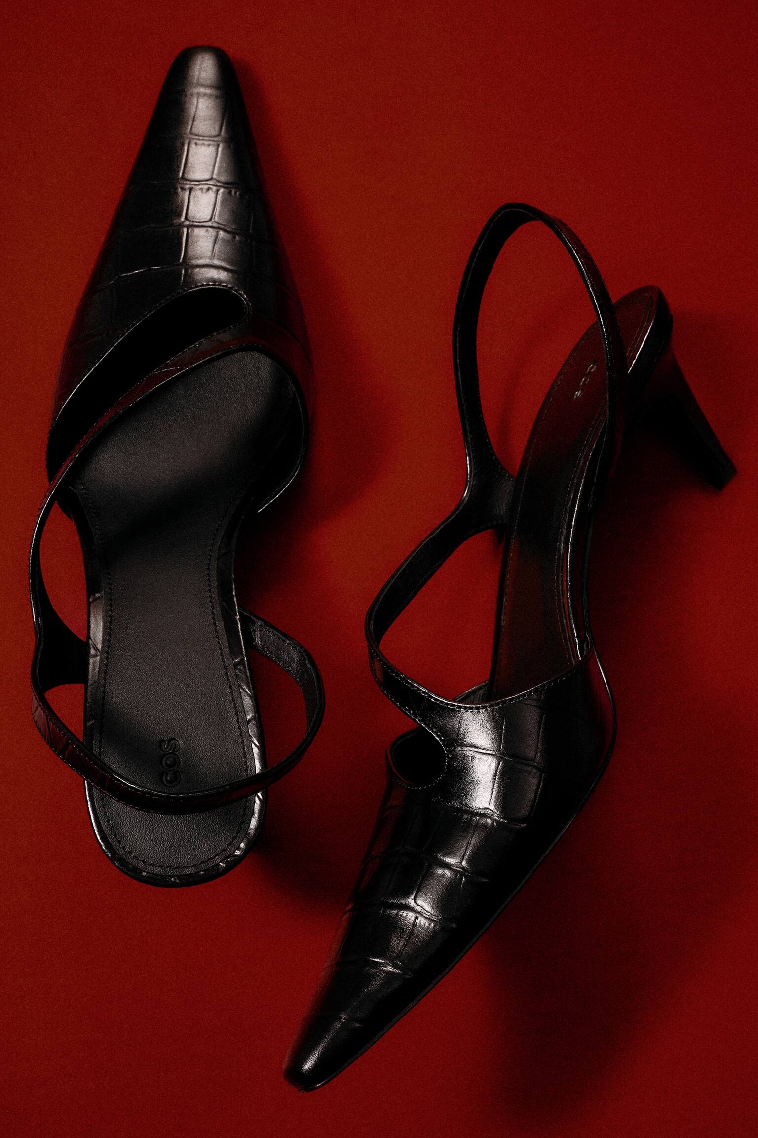 נעלי עקב עם רצועת Slingback מעור במראה קרוק מציגות גימור שחור מבריק ובעל מרקם, עם חרטום מחודד. נעל אחת מונחת שטוחה כדי להציג את הסוליה הפנימית ואת רצועת ה-slingback, בעוד השנייה מונחת על צידה כדי לחשוף את העקב בגובה בינוני ואת פרטי החיתוך הא-סימטריים בחזית הנעל. - 1