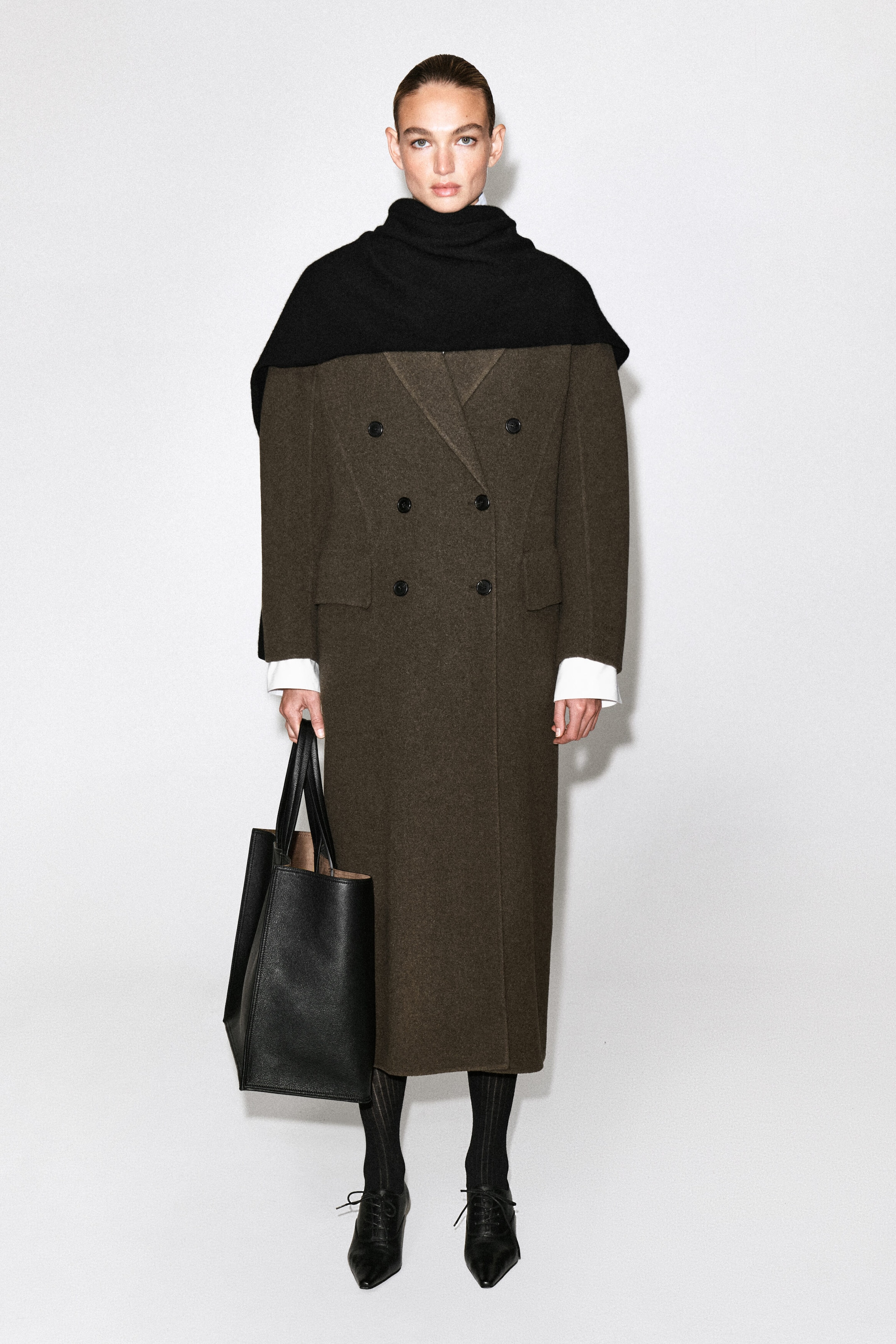 Le modèle porte un manteau en laine olive-brun à double boutonnage, présentant une silhouette longue, des poches à rabat sur le devant et six boutons noirs. Une large écharpe noire est drapée sur les épaules, et un grand sac fourre-tout en cuir noir est tenu dans une main. Le modèle porte un manteau en laine olive-brun à double boutonnage, présentant une silhouette longue, des poches à rabat sur le devant et six boutons noirs. Une large écharpe noire est drapée sur les épaules, et un grand sac fourre-tout en cuir noir est tenu dans une main.