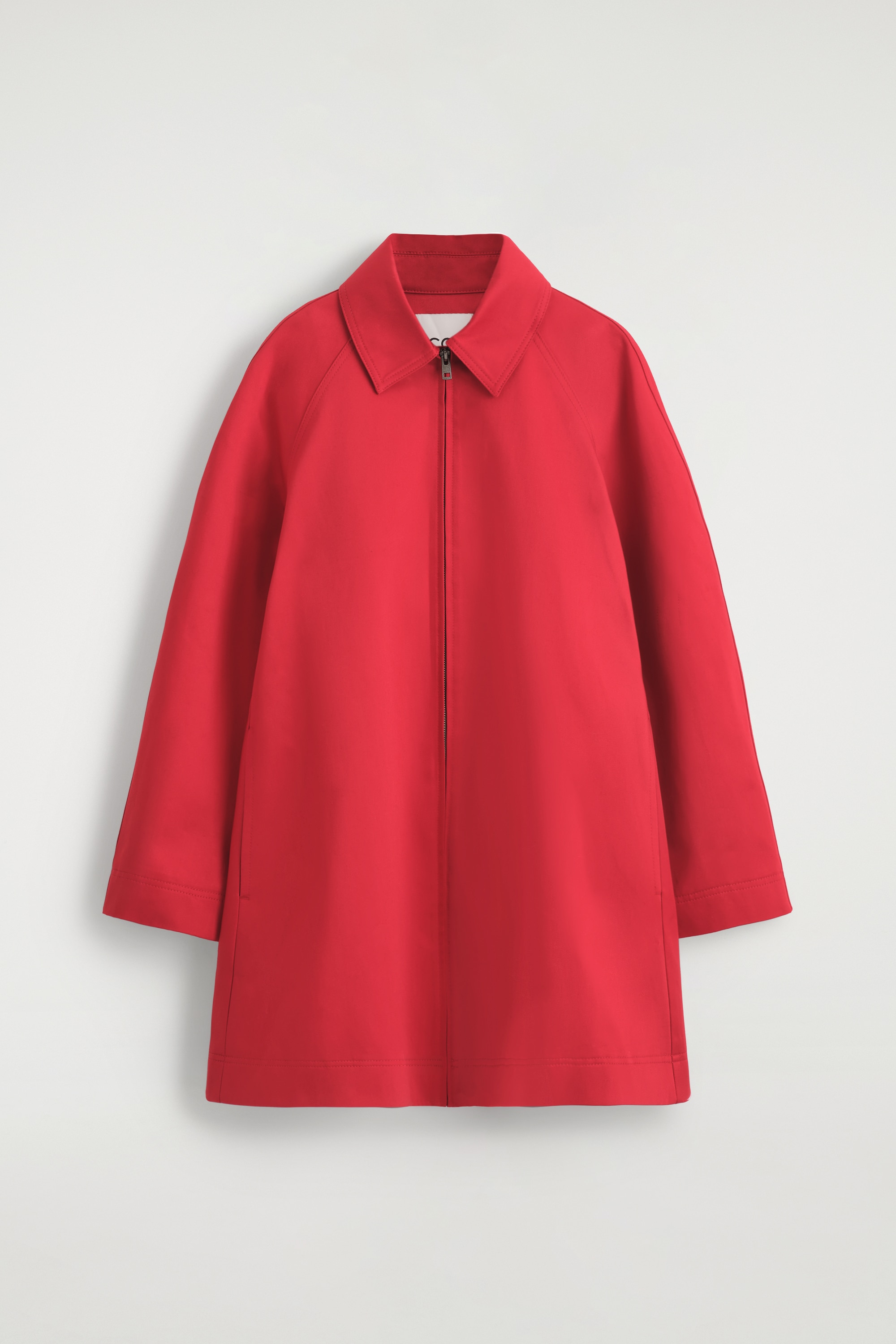 Ce manteau swing sculptural rouge en coton, dotÃ© dâun col pointu, de manches longues et dâune silhouette structurÃ©e en ligne A, est portÃ© par le mannequin. Le manteau est associÃ© Ã  des bottines noires Ã  bout pointu.