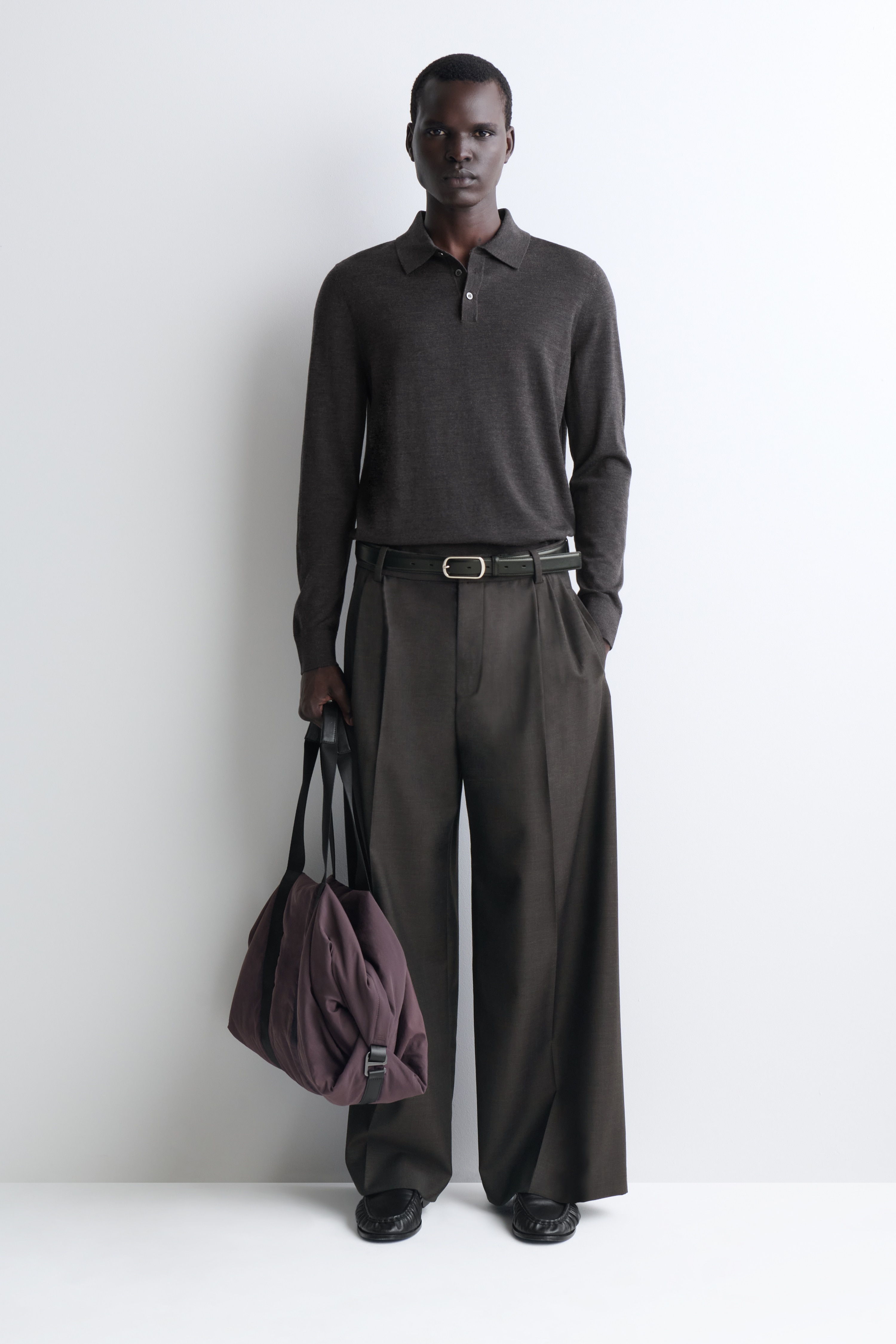Die Nylon-Reisetasche in einem gedeckten Lila steht aufrecht aus einer Frontansicht und zeigt ihren zylindrischen KÃ¶rper sowie zwei breite schwarze Webbing-TrÃ¤ger, die vertikal darum herum verlaufen. Diese TrÃ¤ger fÃ¼hren nach oben zu Tragegriffen, die mit schwarzen Lederdetails veredelt sind.