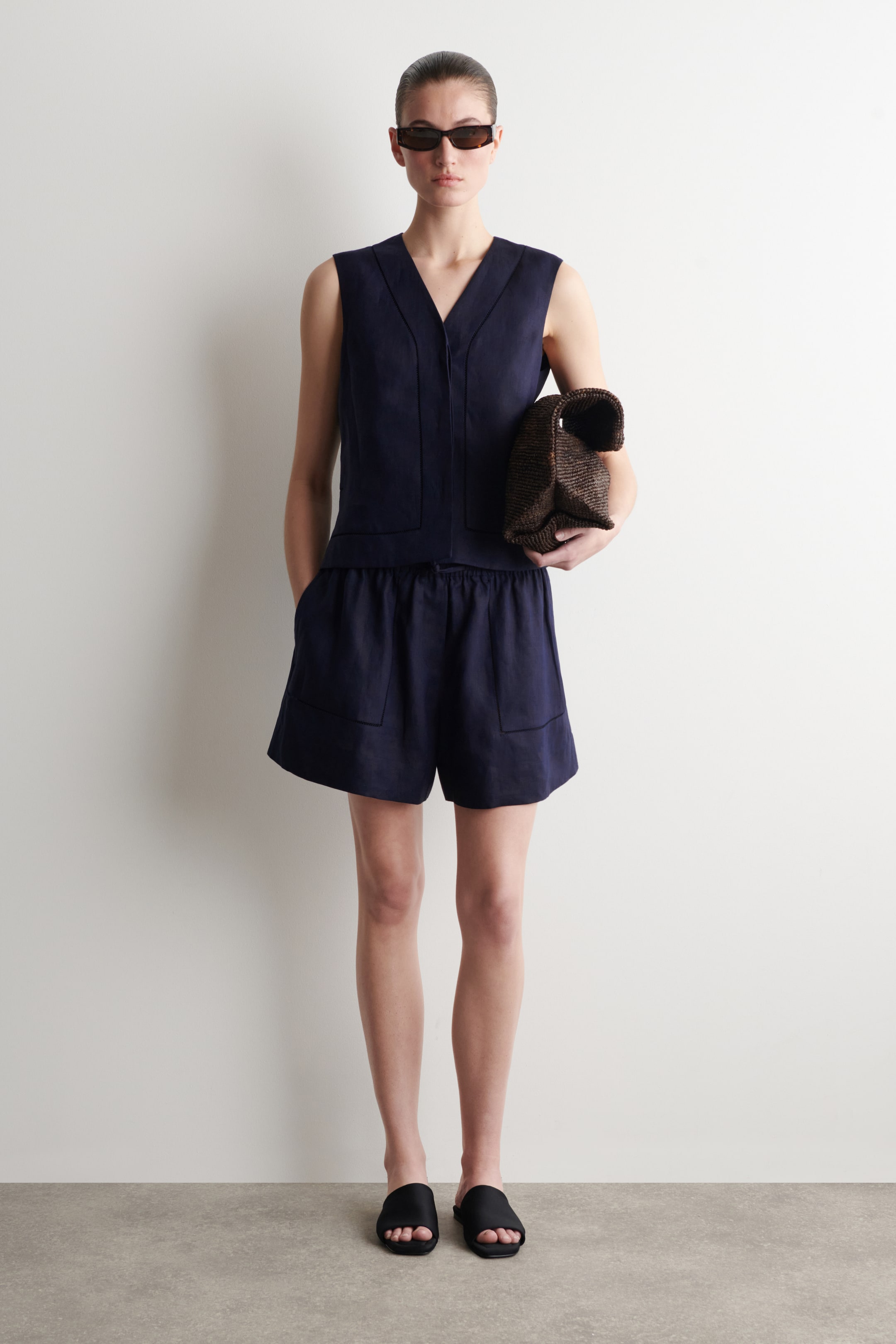 Agrandir l'image: Un ensemble bleu foncé sans manches avec un haut à col en V et un short assorti est présenté de face. Le haut présente un col en V, un panneau vertical et une couture horizontale à la taille, tandis que le short est conçu avec une taille élastiquée et des poches plaquées à l'avant.