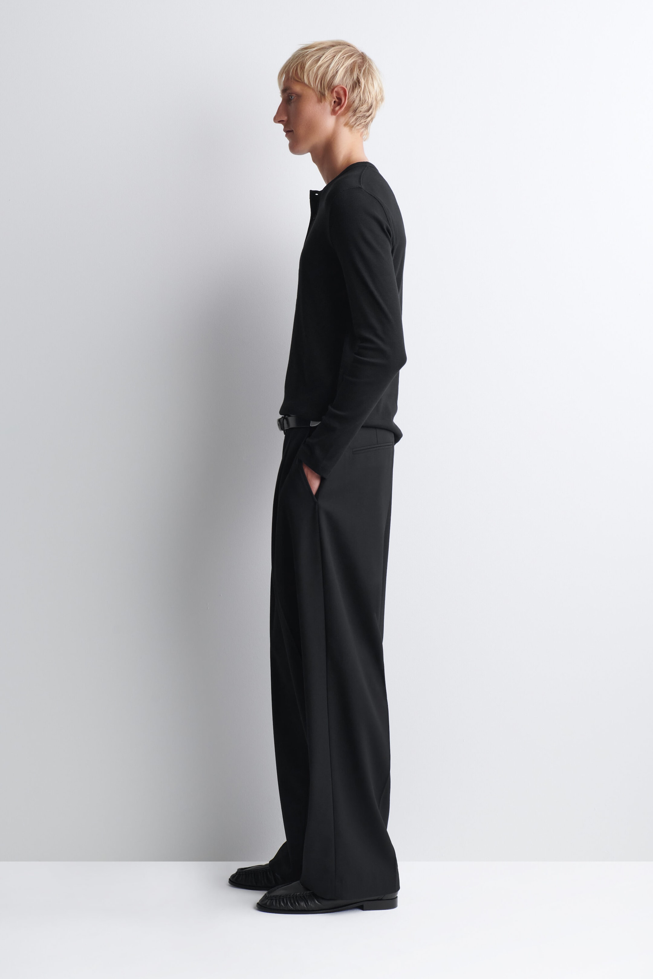 The black slim ribbed cotton long-sleeve henley T-shirt presents a form-fitting silhouette, shown in profile facing right to highlight its clean lines. It features a subtle ribbed texture and is styled tucked into wide-leg black trousers to demonstrate its lightweight drape. The black slim ribbed cotton long-sleeve henley T-shirt presents a form-fitting silhouette, shown in profile facing right to highlight its clean lines. It features a subtle ribbed texture and is styled tucked into wide-leg black trousers to demonstrate its lightweight drape.