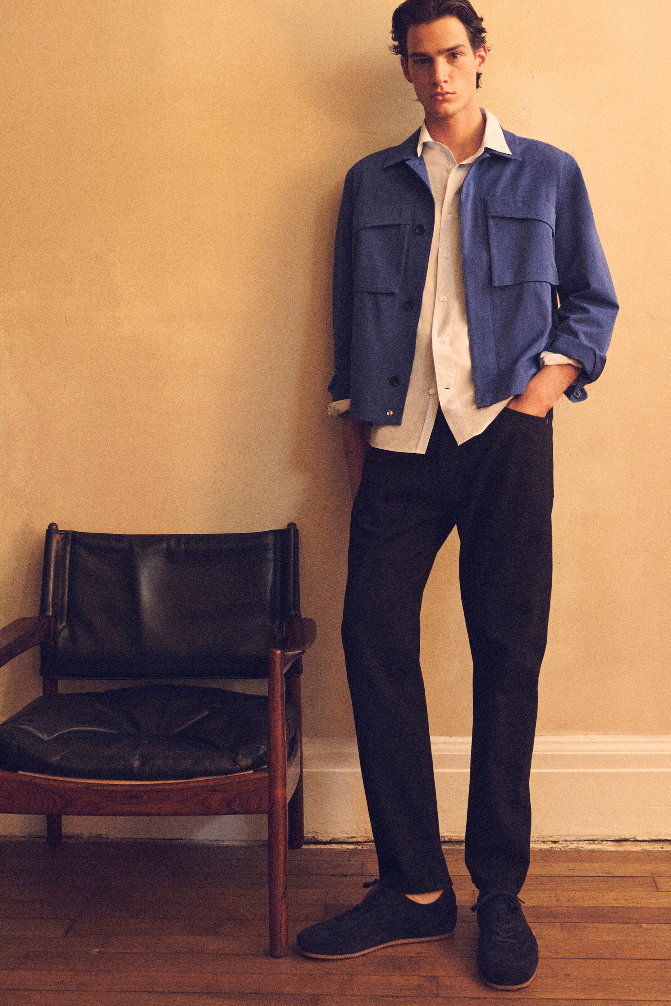 Größeres Bild anzeigen: VORDERSEITE: Ein Modell trägt ein locker sitzendes blaues Overshirt, das offen über einem hellen Hemd getragen wird und mehrere aufgesetzte Taschen sowie einen Knopfverschluss aufweist. Das Modell trägt außerdem eng anliegende dunkelblaue Jeans, die mit einem Fünf-Taschen-Design und silberfarbenen Nieten sichtbar sind.