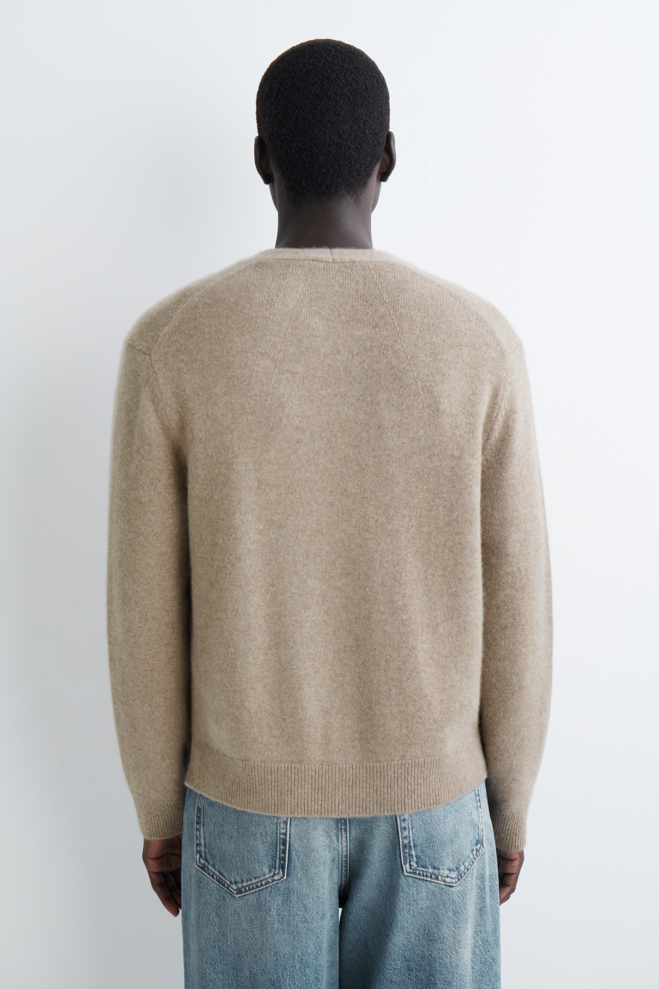 Grotere afbeelding bekijken: Een lichtbeige trui met ronde hals wordt van de achterkant gepresenteerd. Het heeft raglanmouwen en een geribde onderzoom, en wordt gedragen over lichtblauwe jeans.