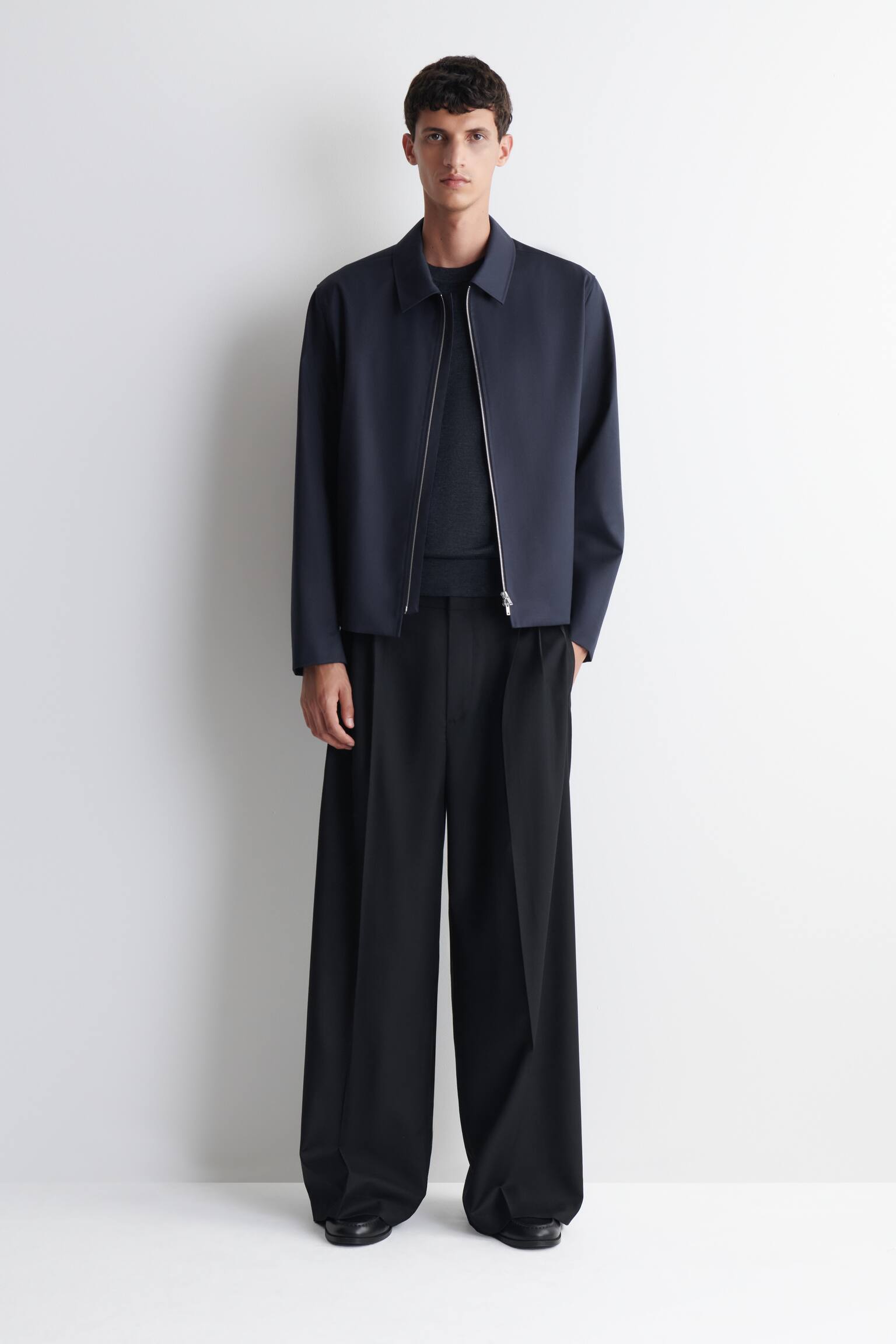 A dark blue jacket is shown with a full-length silver-toned zip down the front. It features a pointed collar and two angled zip pockets on the lower front. - 1