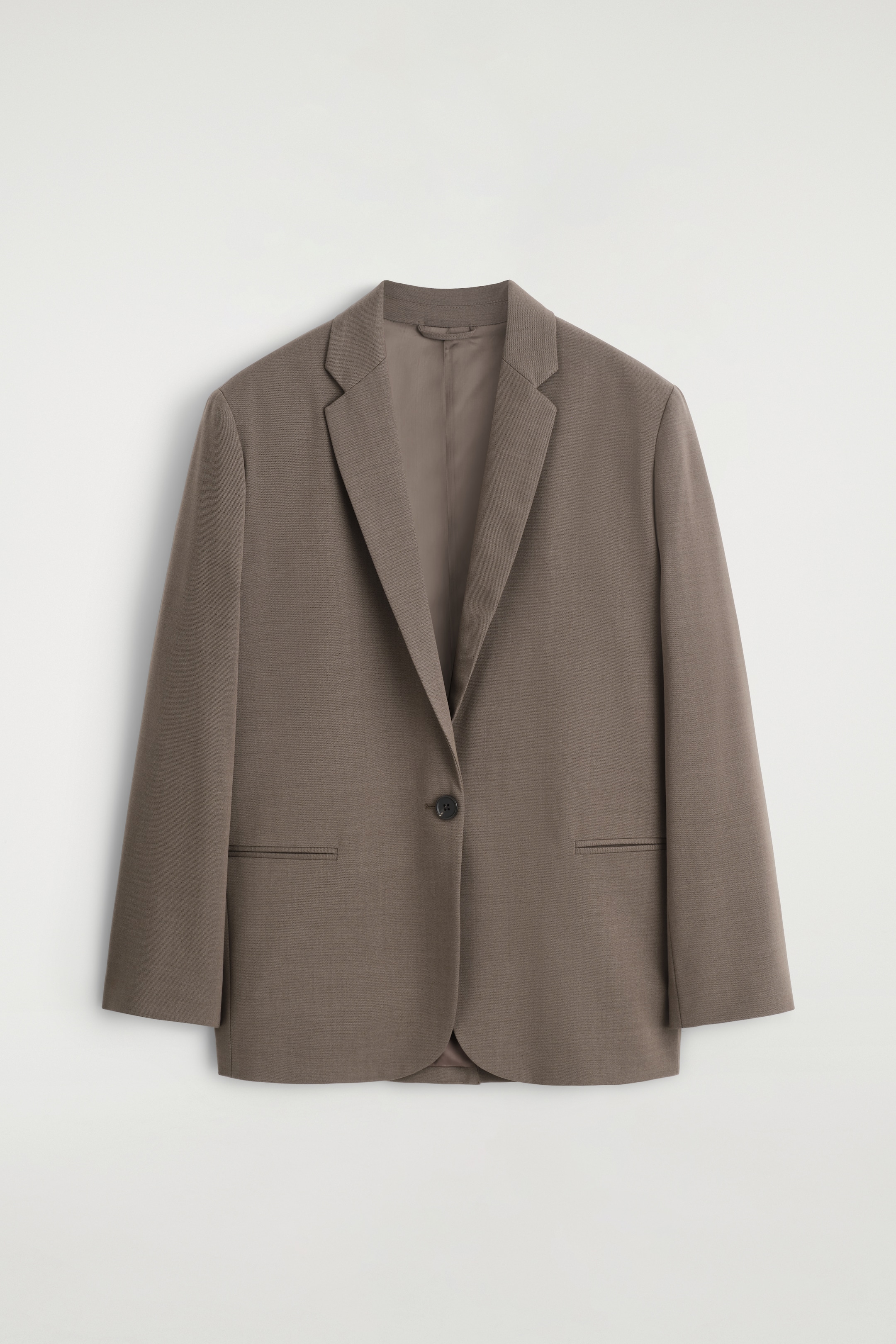 Grösseres Bild ansehen: Ein taupefarbener, einreihiger Blazer präsentiert sich VORNE und erscheint mit einer entspannten Silhouette. Er verfügt über Kerbrevers, einen einzelnen dunklen Knopfverschluss und zwei horizontale Leistentaschen, alles auf einem glatten, fein strukturierten Stoff.