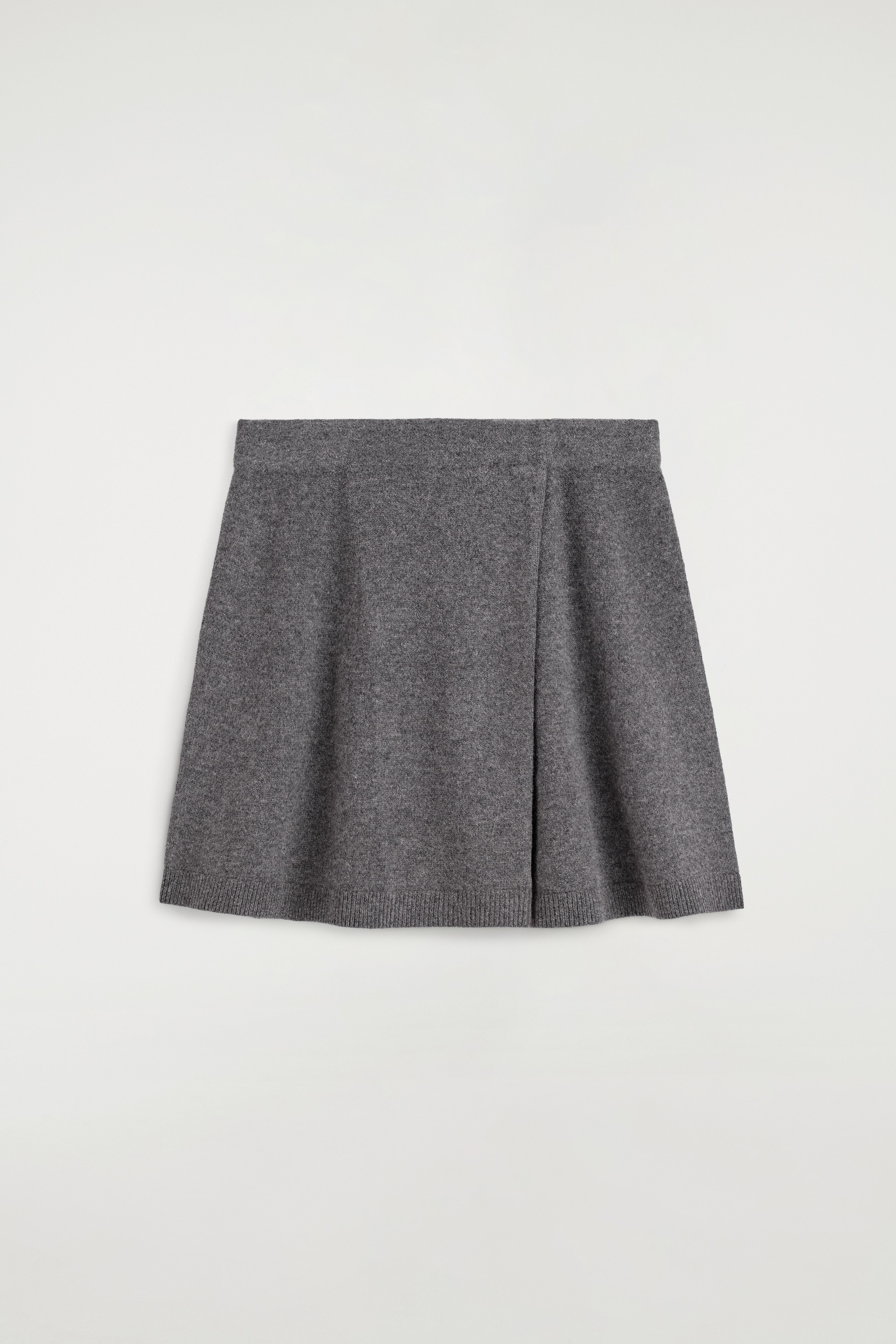 Koszulka polo z weÅny merino i dopasowana mini spÃ³dnica kopertowa sÄ pokazane z przodu, stylizowane razem jako zestaw. Koszulka polo ma swobodny fason, klasyczny koÅnierzyk, listwÄ z guzikami i podwiniÄte rÄkawy, noszona na biaÅej koszuli, natomiast mini spÃ³dnica kopertowa z wysokim stanem prezentuje siÄ w fasonie A z zachodzÄcym na siebie przodem.