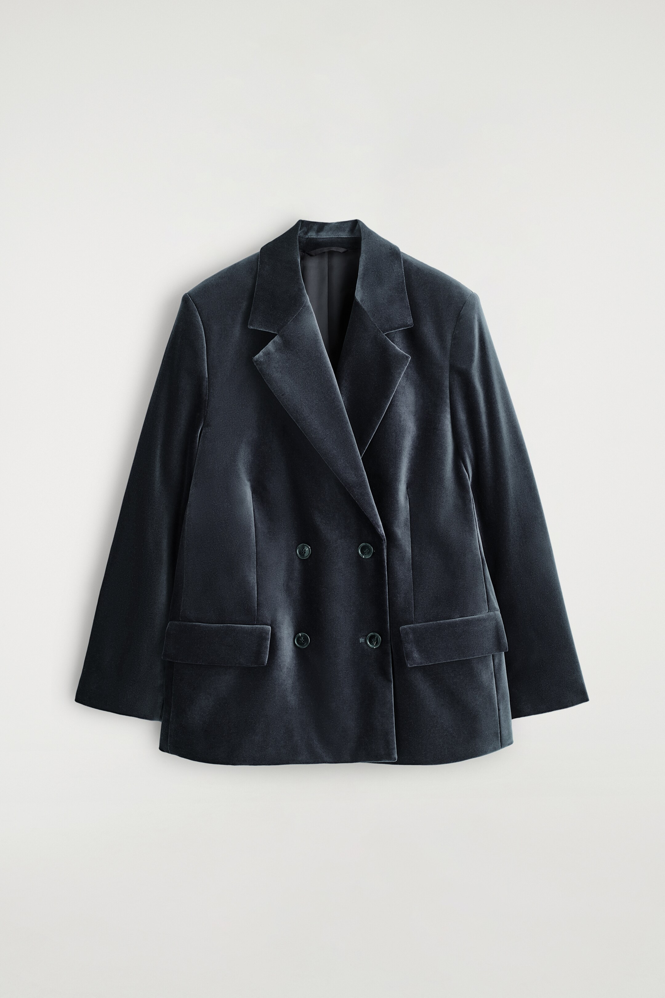 Visualizza immagine più grande: Un blazer doppiopetto in velluto blu scuro è presentato rivolto verso la PARTE ANTERIORE, caratterizzato da revers a dente, quattro bottoni scuri e due tasche frontali a patta.