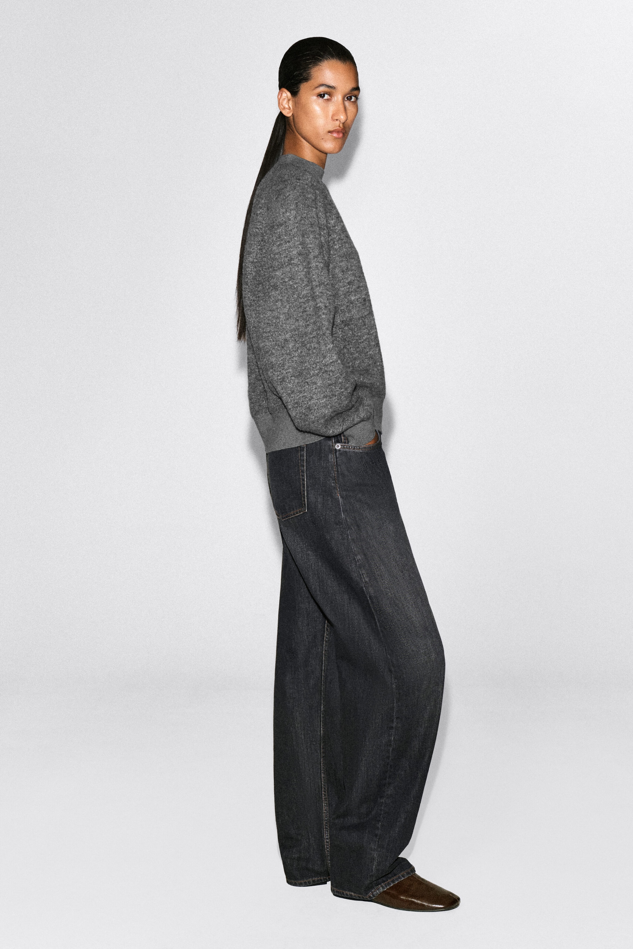 A gray mélange crewneck sweater and dark wash, wide-leg denim jeans are being modeled in profile, facing right. The relaxed-fit sweater features ribbed trim at the neck, cuffs, and hem, while the jeans drape loosely over dark brown slip-on shoes. A gray mélange crewneck sweater and dark wash, wide-leg denim jeans are being modeled in profile, facing right. The relaxed-fit sweater features ribbed trim at the neck, cuffs, and hem, while the jeans drape loosely over dark brown slip-on shoes.