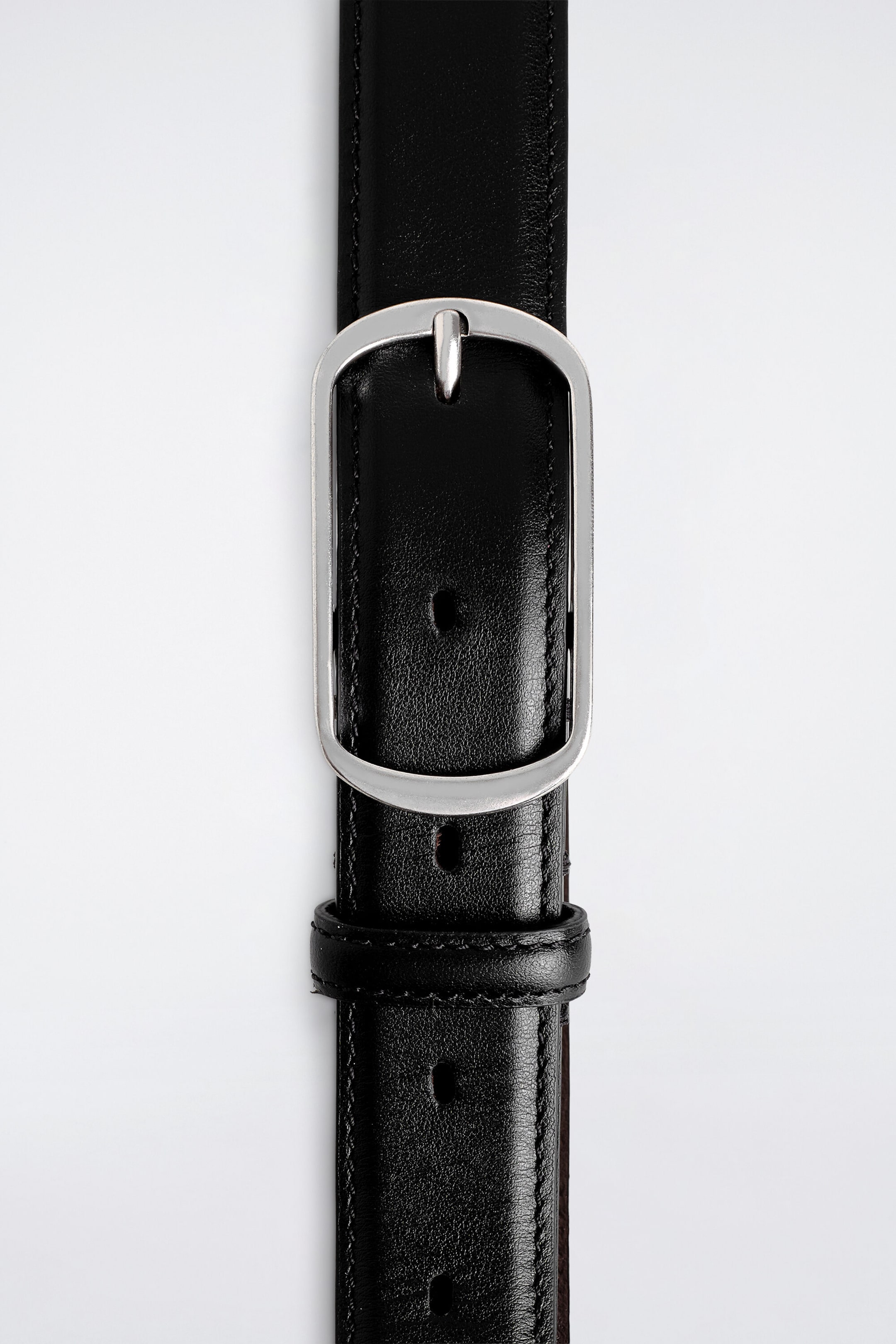 A curved-buckle leather belt extends vertically from the front, showcasing its smooth black leather strap with fine edge stitching. The strap is secured through a rounded, silver-toned rectangular buckle and passes through a matching black leather keeper loop. A curved-buckle leather belt extends vertically from the front, showcasing its smooth black leather strap with fine edge stitching. The strap is secured through a rounded, silver-toned rectangular buckle and passes through a matching black leather keeper loop.