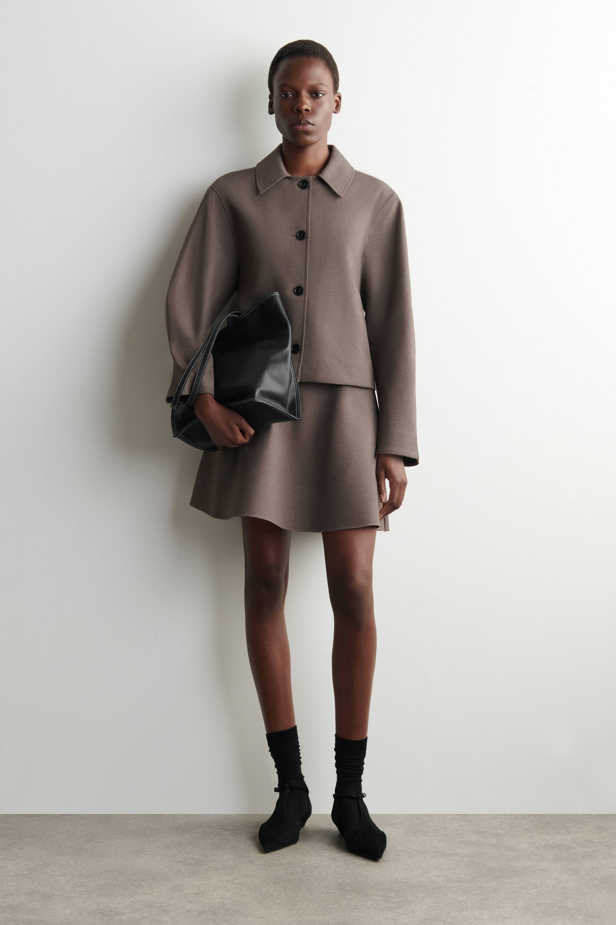 Größeres Bild ansehen: Ein dezenter brauner Minirock zeigt eine ausgestellte Silhouette und ein glattes, sauberes Finish, getragen mit der Vorderseite nach vorne.