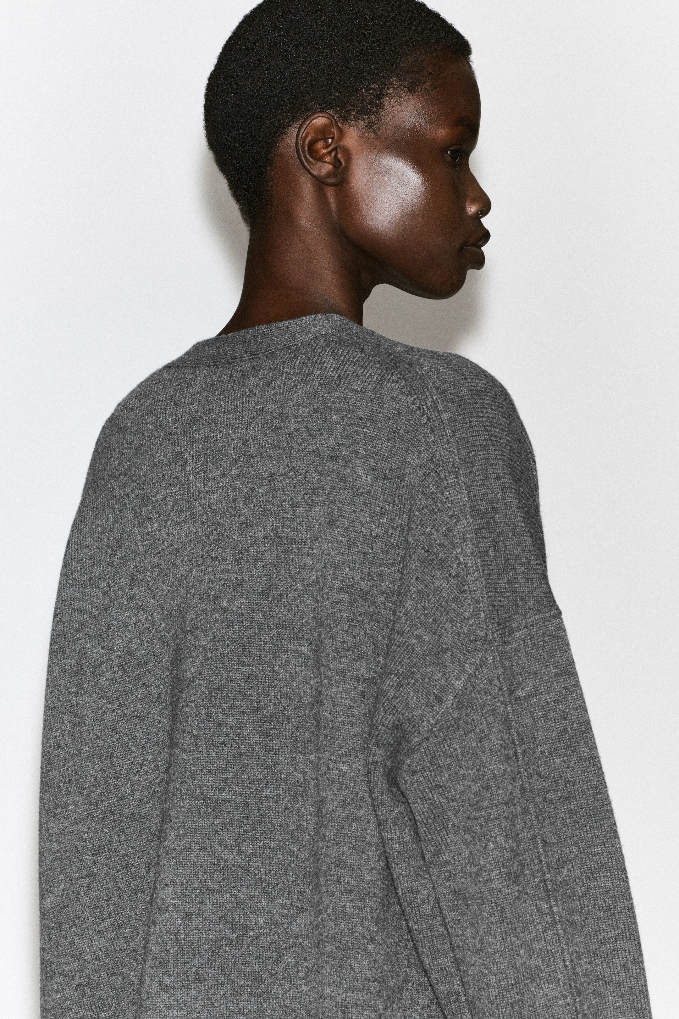 Un cardigan in maglia grigia è indossato dalla modella, mettendone in risalto la vestibilità rilassata e le spalle scese in una vista di profilo posteriore. Il capo presenta una texture a maglia fine e un bordo a coste lungo lo scollo posteriore. Un cardigan in maglia grigia è indossato dalla modella, mettendone in risalto la vestibilità rilassata e le spalle scese in una vista di profilo posteriore. Il capo presenta una texture a maglia fine e un bordo a coste lungo lo scollo posteriore.