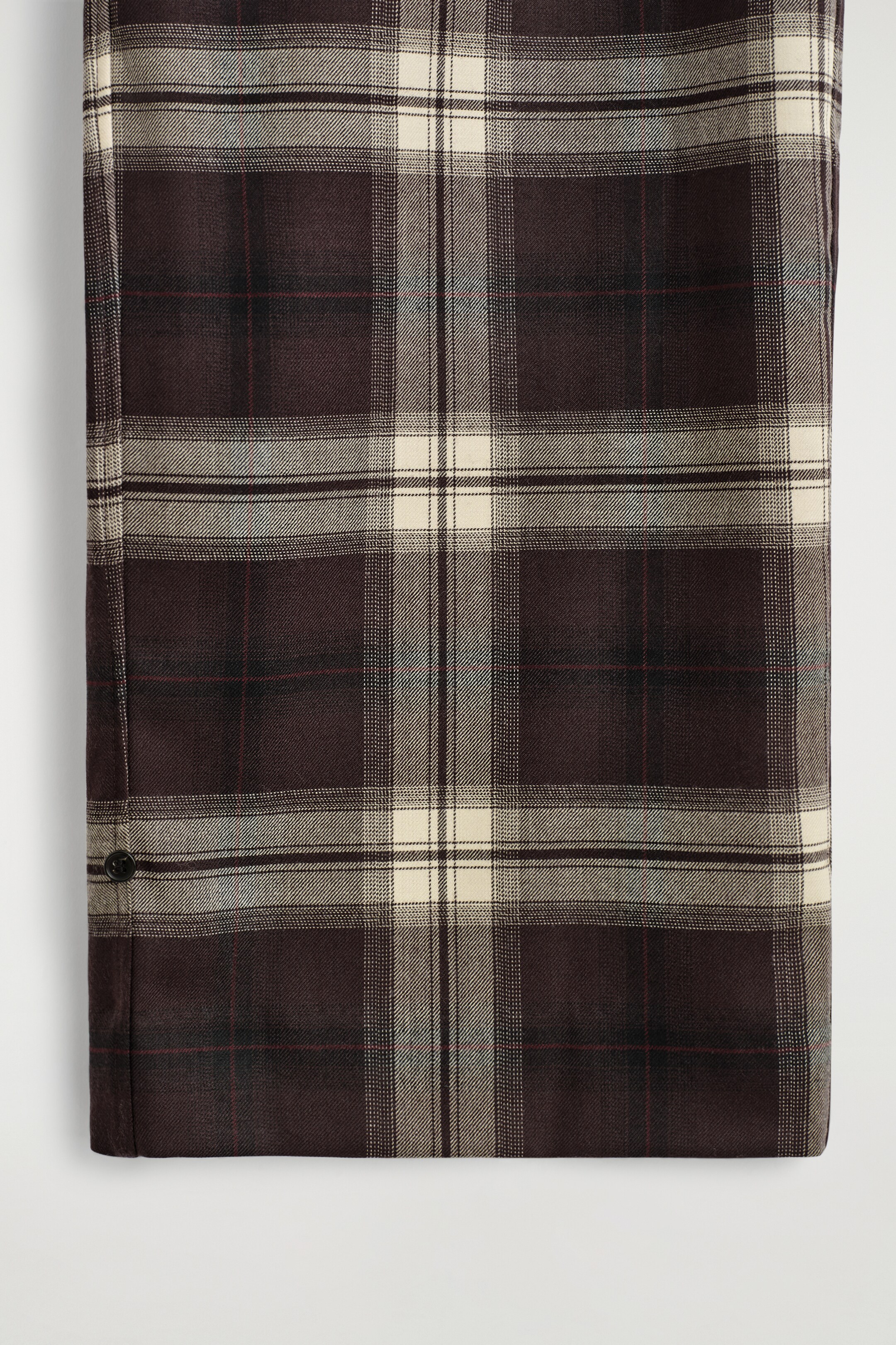 Agrandir l'image: Le pantalon affiche un motif à carreaux tissés en marron foncé, beige et gris, rehaussé de fines lignes rouges et de subtiles lignes bleues, avec un bouton sombre apparaissant sur le côté inférieur gauche.