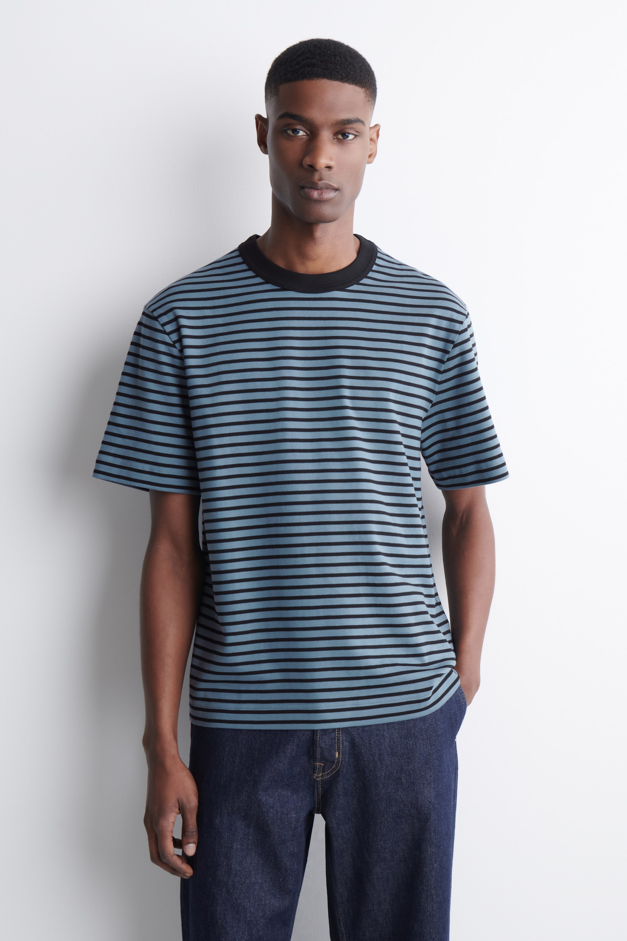 Grösseres Bild ansehen: Das T-Shirt ist mit hellblauen und schwarzen horizontalen Streifen versehen. Es ist mit einem schwarzen, gerippten Rundhalsausschnitt und kurzen Ärmeln gestaltet und präsentiert sich von vorne in einer lockeren Passform.