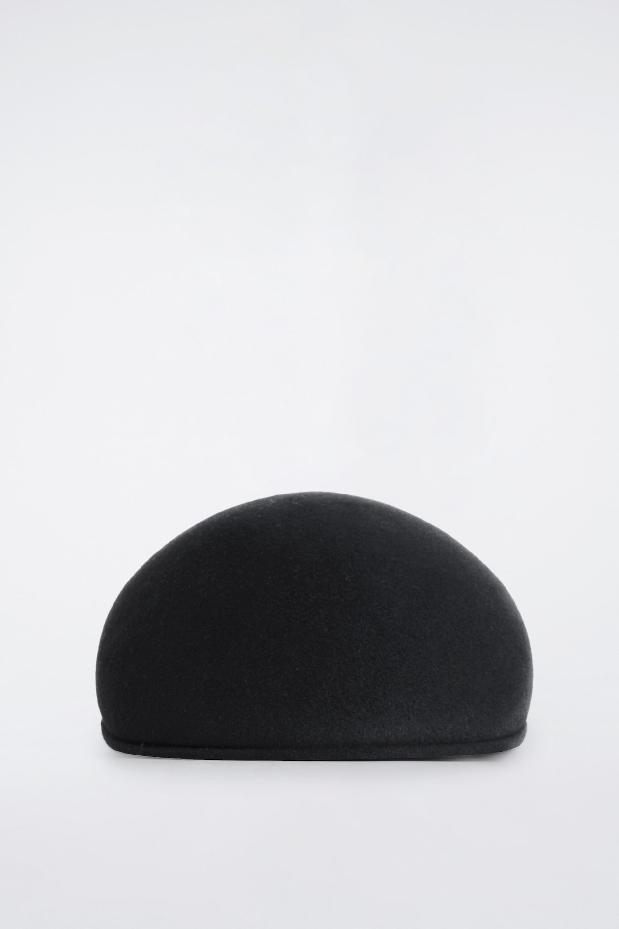 Une casquette plate noire en laine bouillie repose sur une surface, présentant sa silhouette arrière nette, sans couture et arrondie.