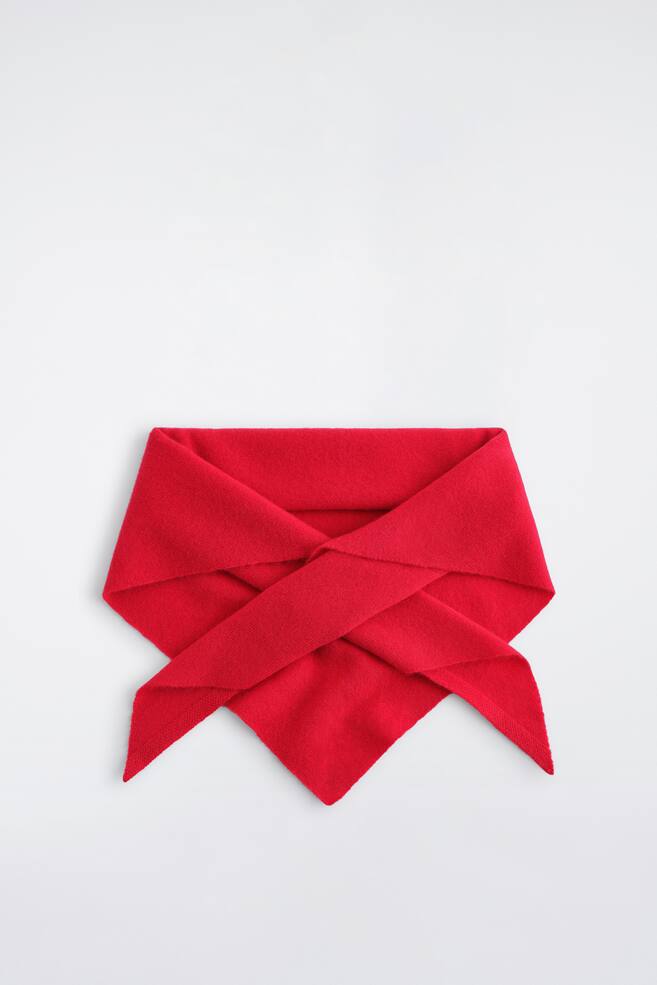A red triangle scarf lies flat, folded with its ends crossed over the front, creating a layered effect that tapers to a central point. The cashmere fabric showcases a soft, fine knit texture. - 1