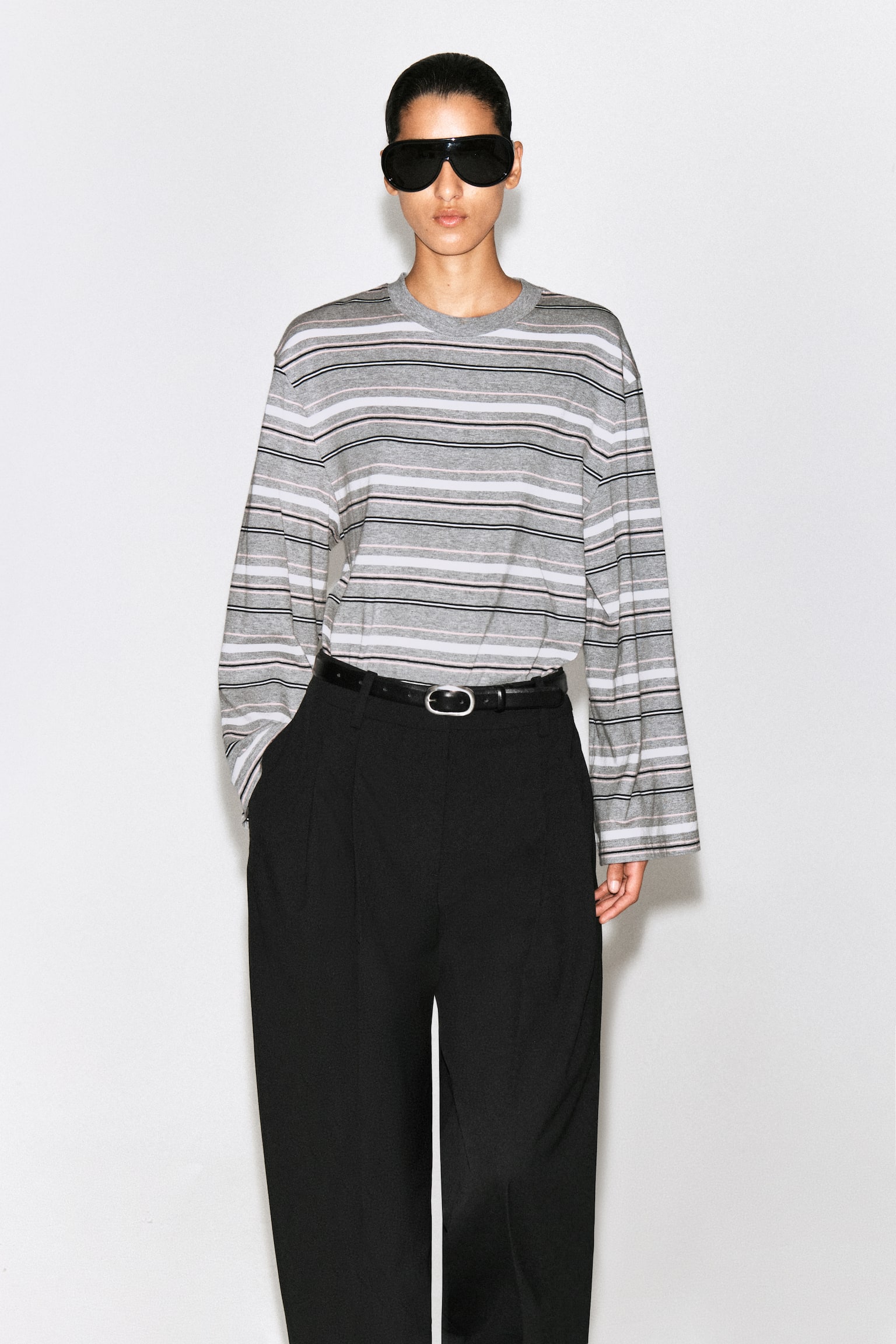 A brushed-cotton long-sleeved T-shirt is shown facing front, featuring a horizontal striped pattern in grey, white, black, and light pink. The top has a relaxed fit with a ribbed crew neck, dropped shoulders, and wide, straight-cut sleeves. - 1