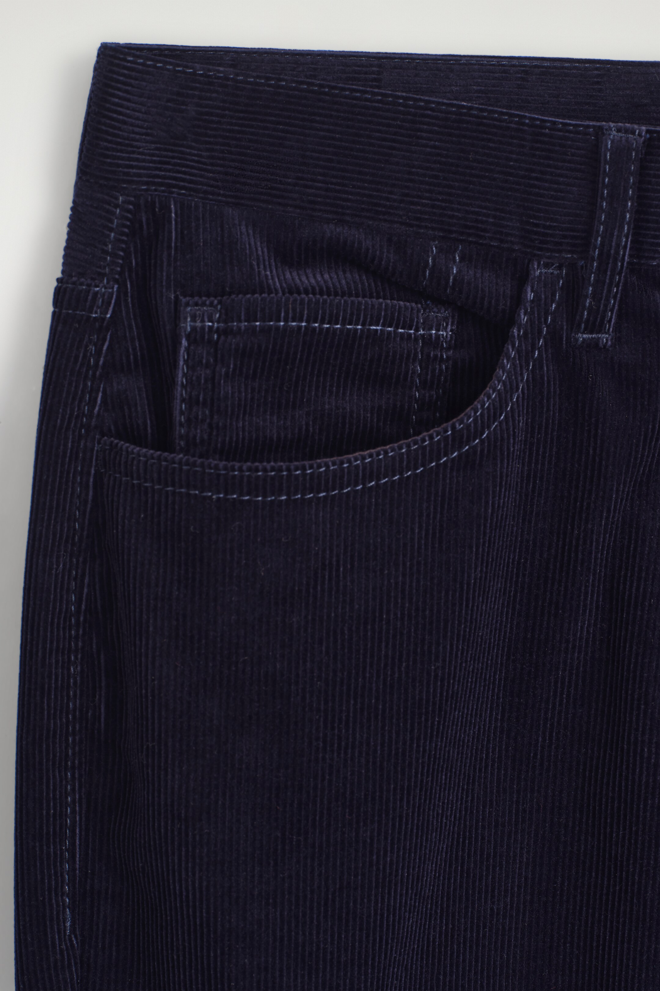 Agrandir l'image: Un pantalon en velours côtelé bleu foncé présente une ceinture visible, un passant de ceinture et une poche avant incurvée avec une poche à monnaie intérieure, le tout détaillé avec des coutures contrastées claires le long des bords des poches, de la couture latérale et de la ceinture.