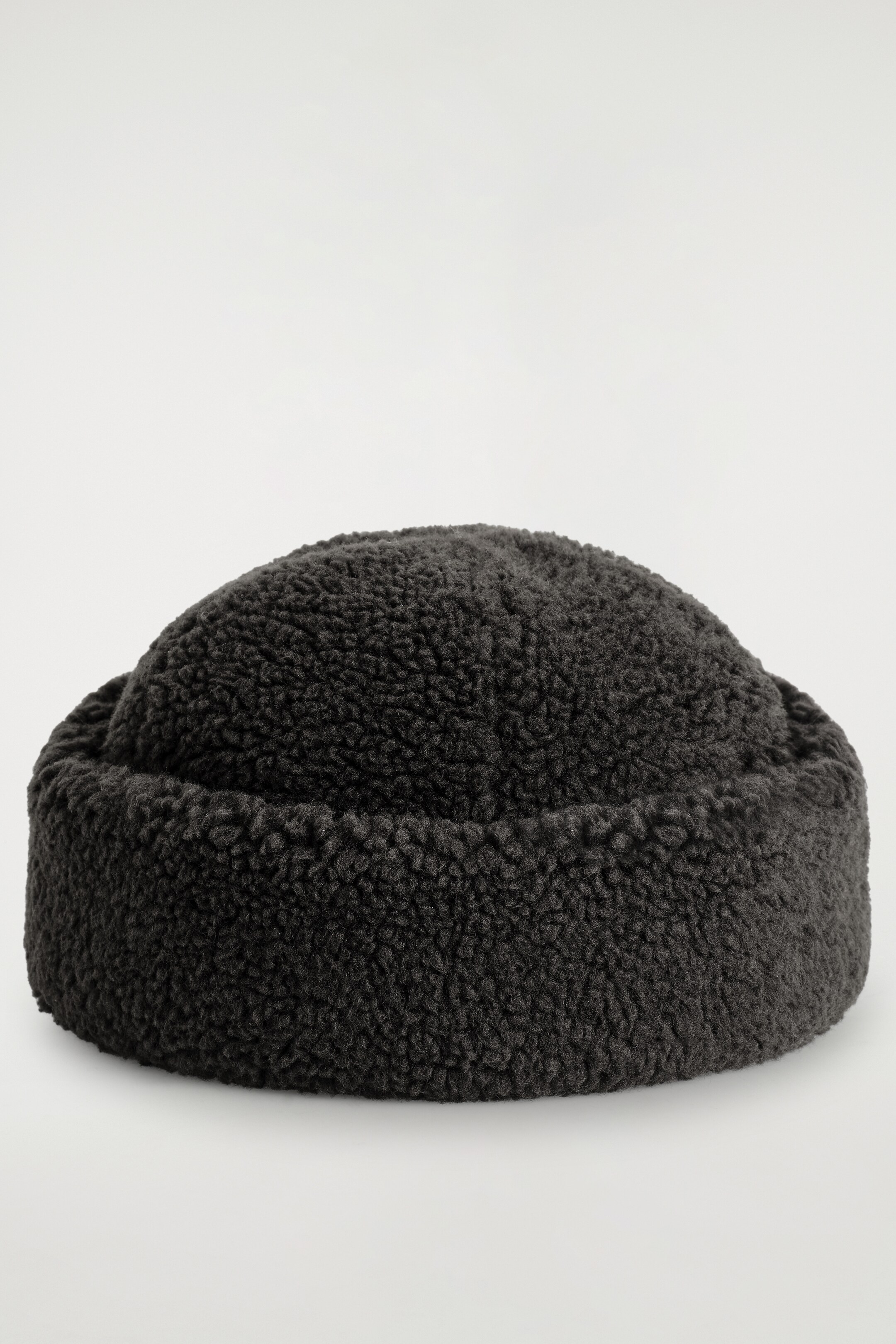 View larger image: A dark gray sherpa hat is featuring a rounded crown and a thick, turned-up brim. The hat is presenting a uniform, curly textured surface.