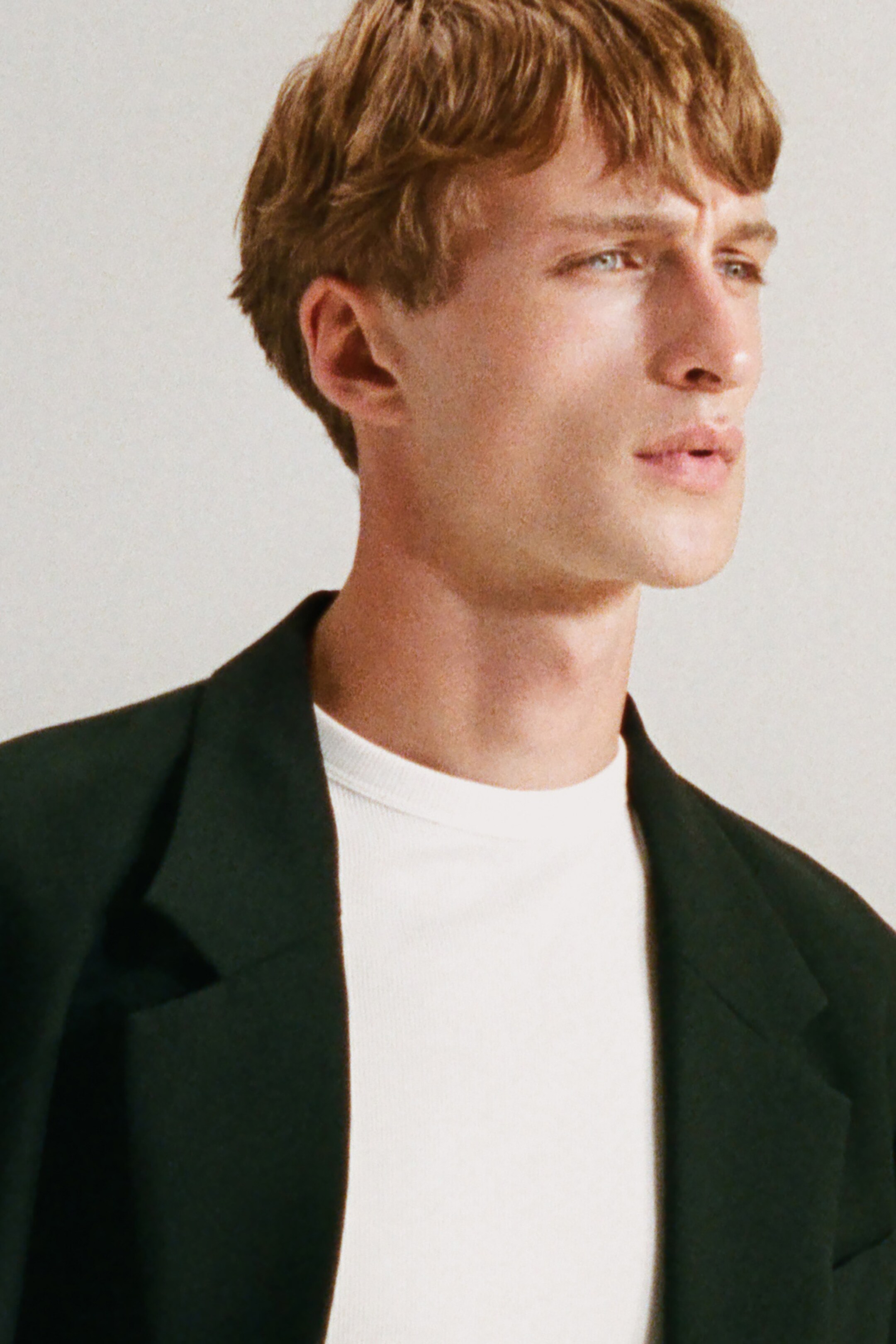 Agrandir l'image: Un blazer de couleur sombre, avec des revers crantés et une coupe décontractée et non structurée au niveau des épaules, est porté par-dessus un t-shirt blanc à col rond côtelé.