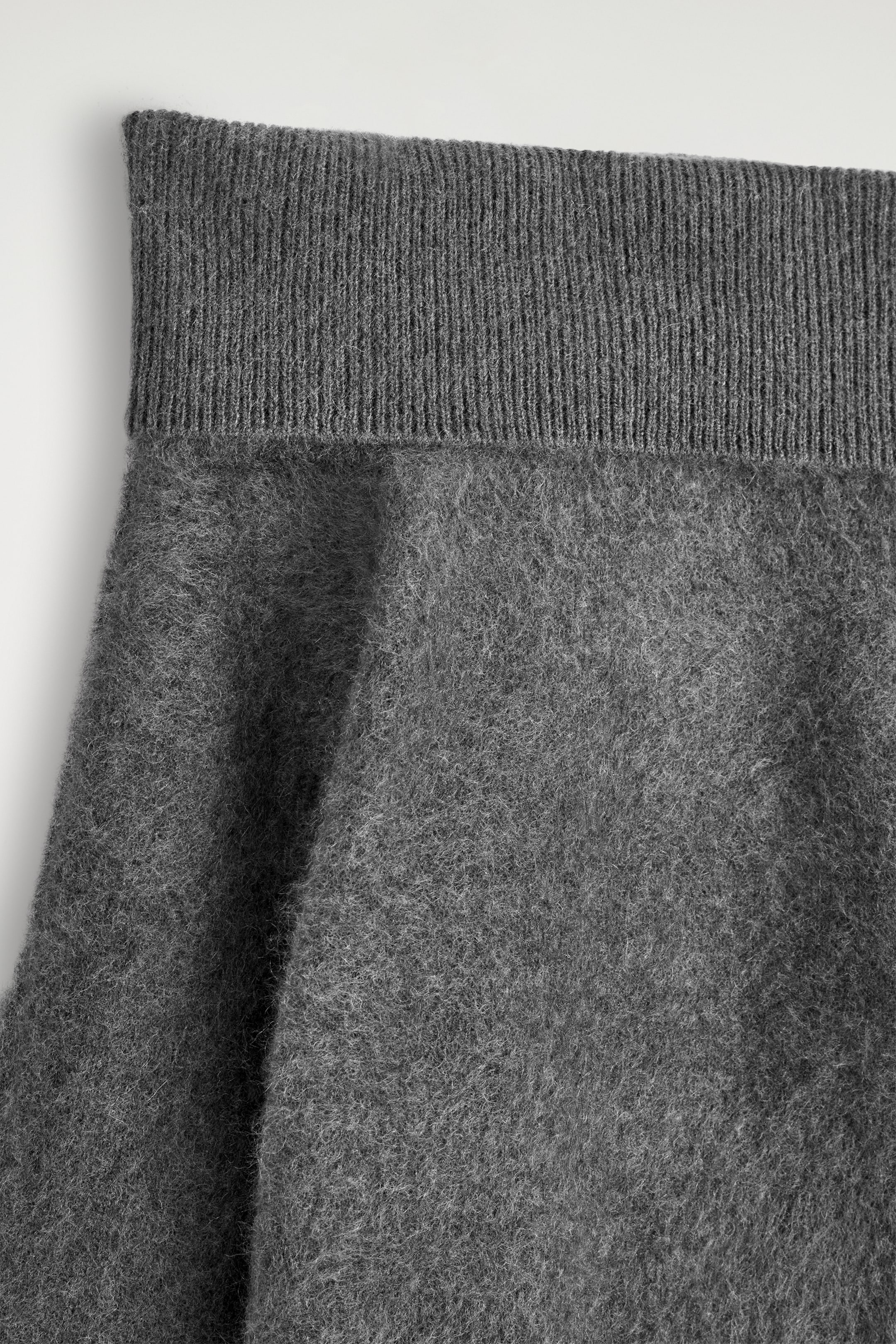 Ver imagen más grande: Un jersey gris de punto presenta una textura cepillada y peluda en su cuerpo principal. El borde superior muestra una banda ancha, doblada y acanalada.