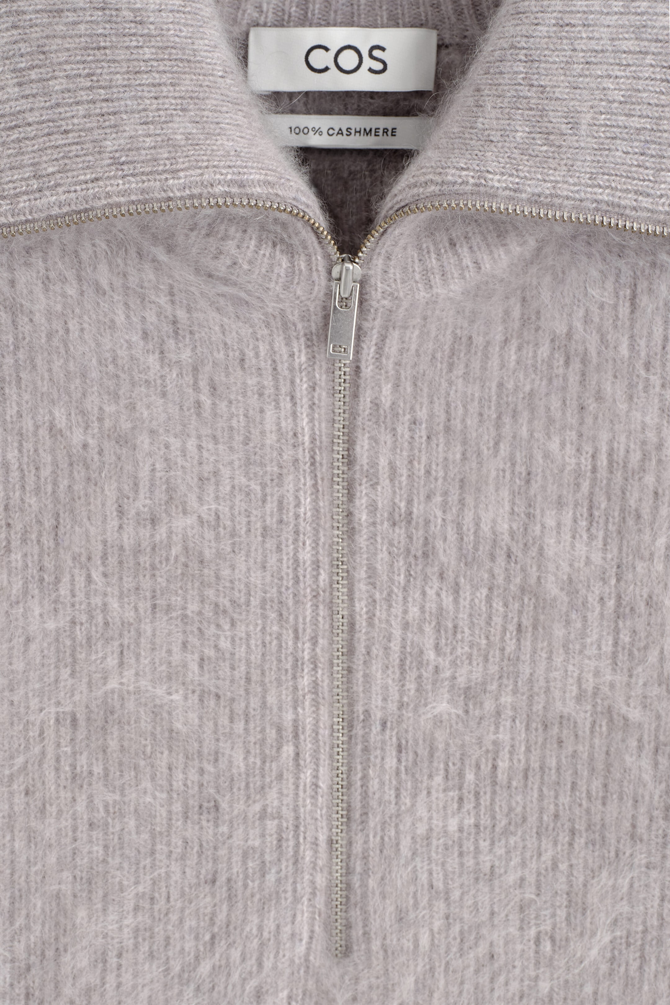 A gray cashmere sweater displays a fuzzy, brushed texture and a silver-tone half-zip closure at the ribbed collar in a close-up front view. A gray cashmere sweater displays a fuzzy, brushed texture and a silver-tone half-zip closure at the ribbed collar in a close-up front view.