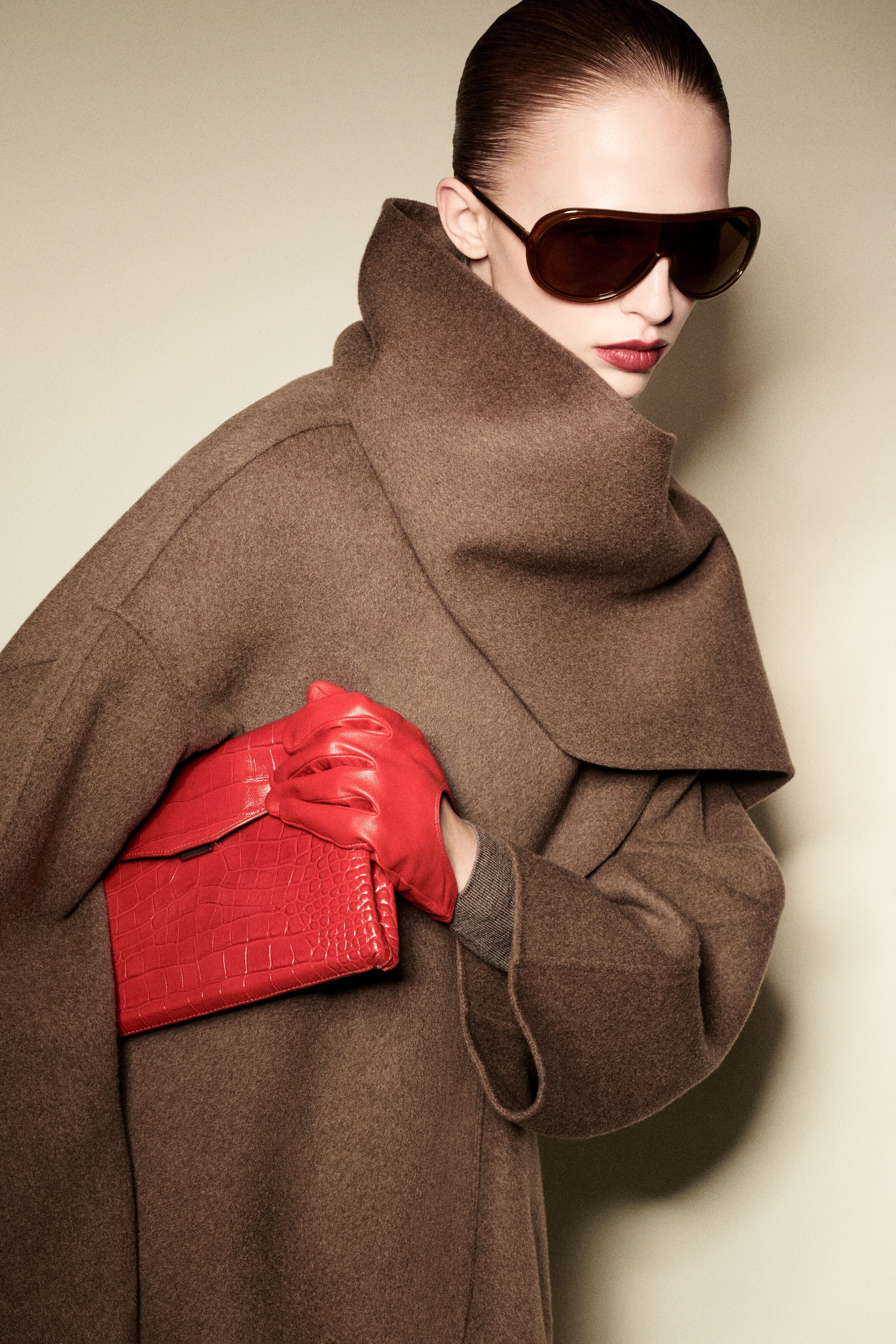 A model facing front-right is wearing a brown double-faced wool-blend scarf jacket featuring a high, draped built-in scarf collar and wide, relaxed sleeves. She is holding a vibrant red croc-effect leather envelope clasp pouch tucked under her arm, styled with matching red leather gloves. A model facing front-right is wearing a brown double-faced wool-blend scarf jacket featuring a high, draped built-in scarf collar and wide, relaxed sleeves. She is holding a vibrant red croc-effect leather envelope clasp pouch tucked under her arm, styled with matching red leather gloves.