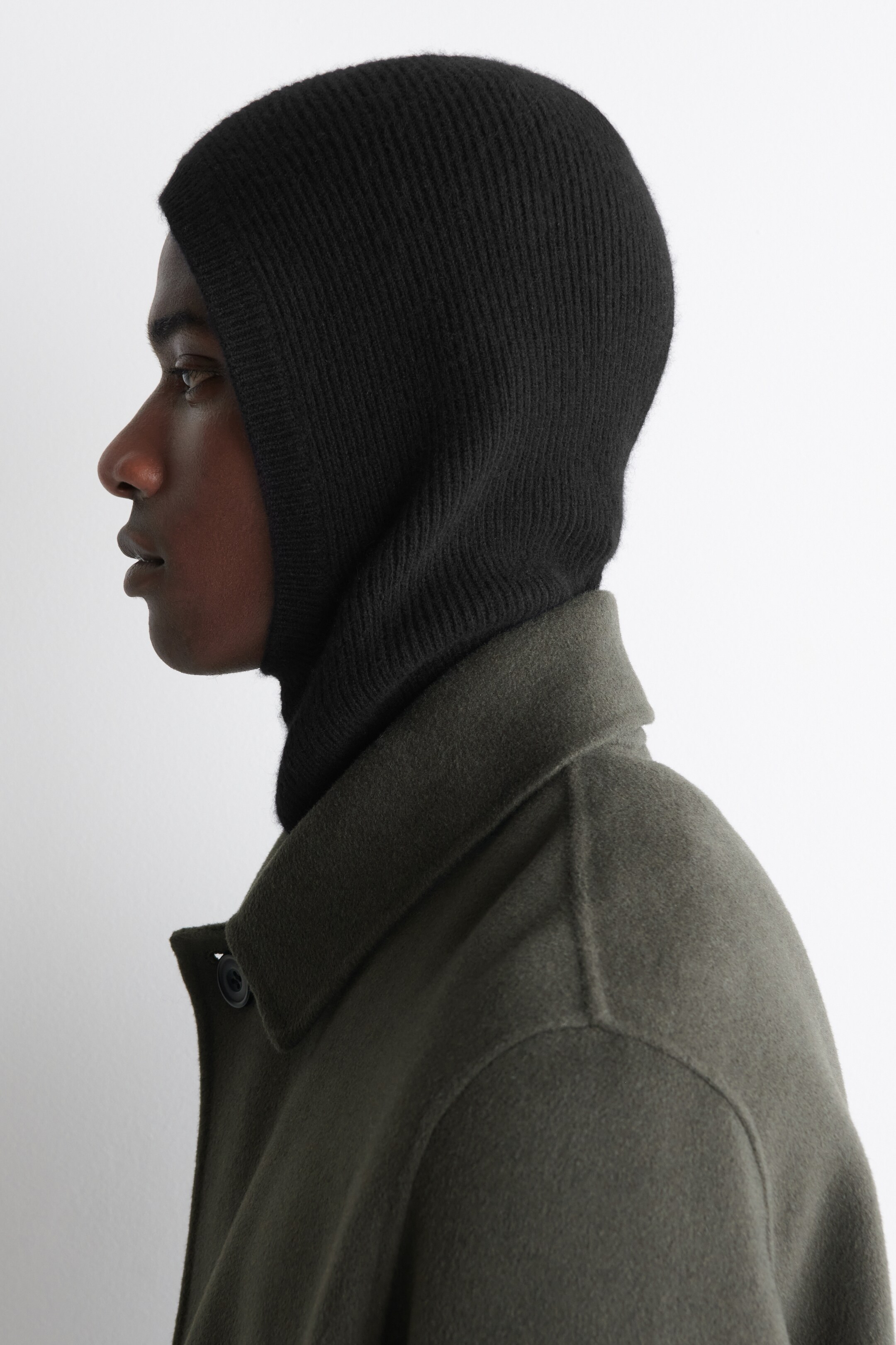 View larger image: A black rib-knit balaclava is covering the model's head and neck, and is being layered under a dark green coat.
