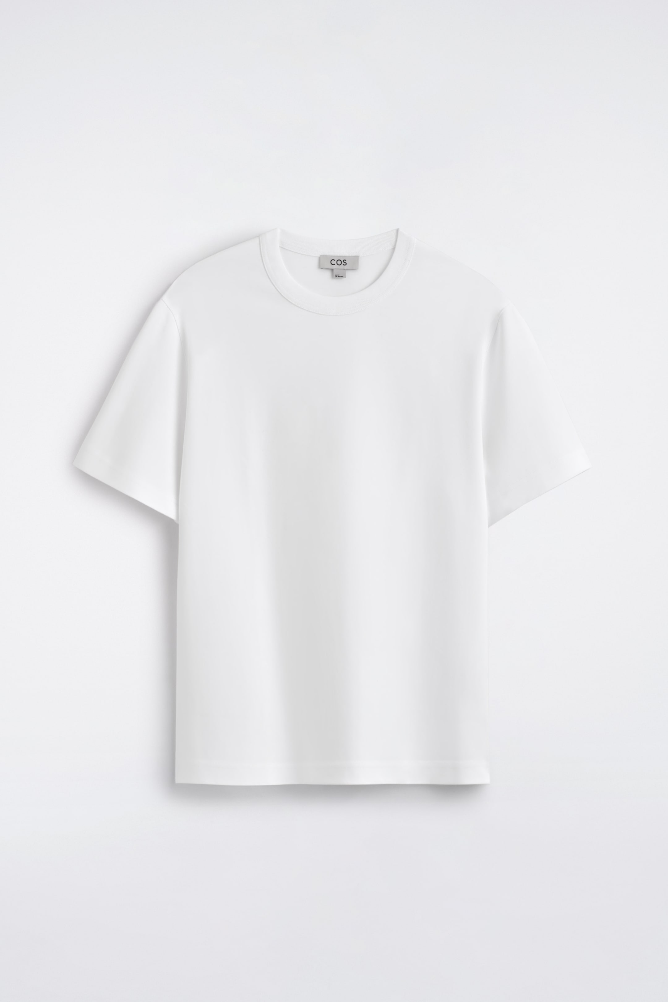 Ver imagen más grande: Se presenta una camiseta blanca de manga corta de frente. Cuenta con un cuello redondo, un dobladillo recto y un ajuste holgado, y una pequeña etiqueta de la marca se muestra en la parte posterior del cuello.