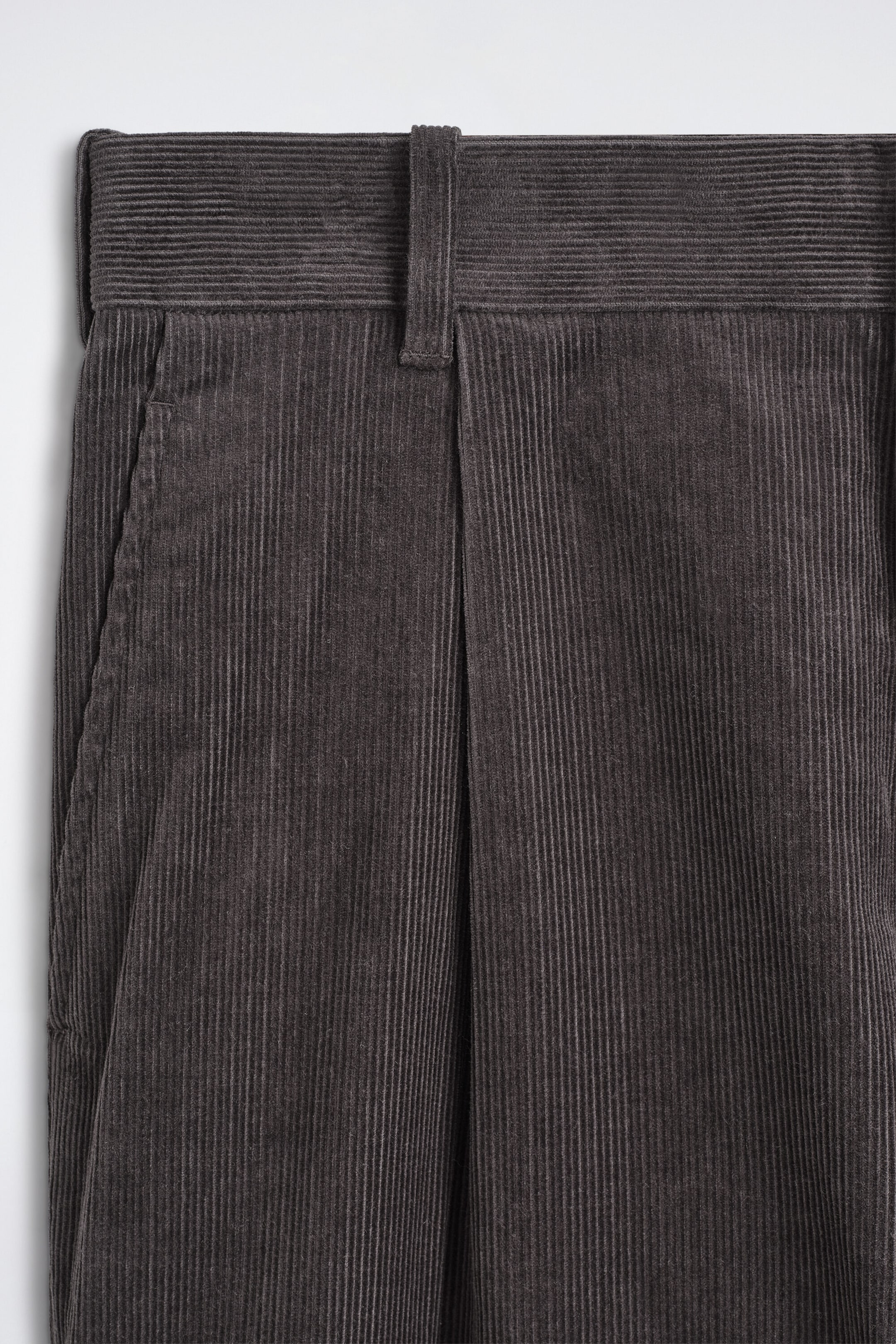 The corduroy relaxed-fit tapered pants are shown in a close-up front view, showcasing a dark gray ribbed texture, a structured waistband with belt loops, a single front pleat, and a side slip pocket. The corduroy relaxed-fit tapered pants are shown in a close-up front view, showcasing a dark gray ribbed texture, a structured waistband with belt loops, a single front pleat, and a side slip pocket.