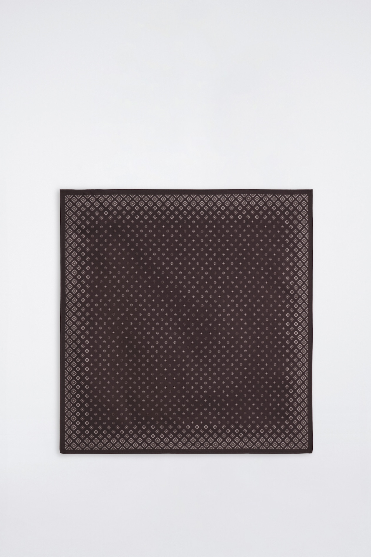 Ein quadratisches Einstecktuch in Dunkelbraun liegt flach und zeigt seine Vorderseite mit einem wiederholenden, hellbeigen geometrischen Mikro-Muster. Das Design weist kleine, gleichmässig verteilte Rauten-Motive über die gesamte Fläche sowie einen dichteren, mehrreihigen Rautenrand entlang der äusseren Kanten auf.